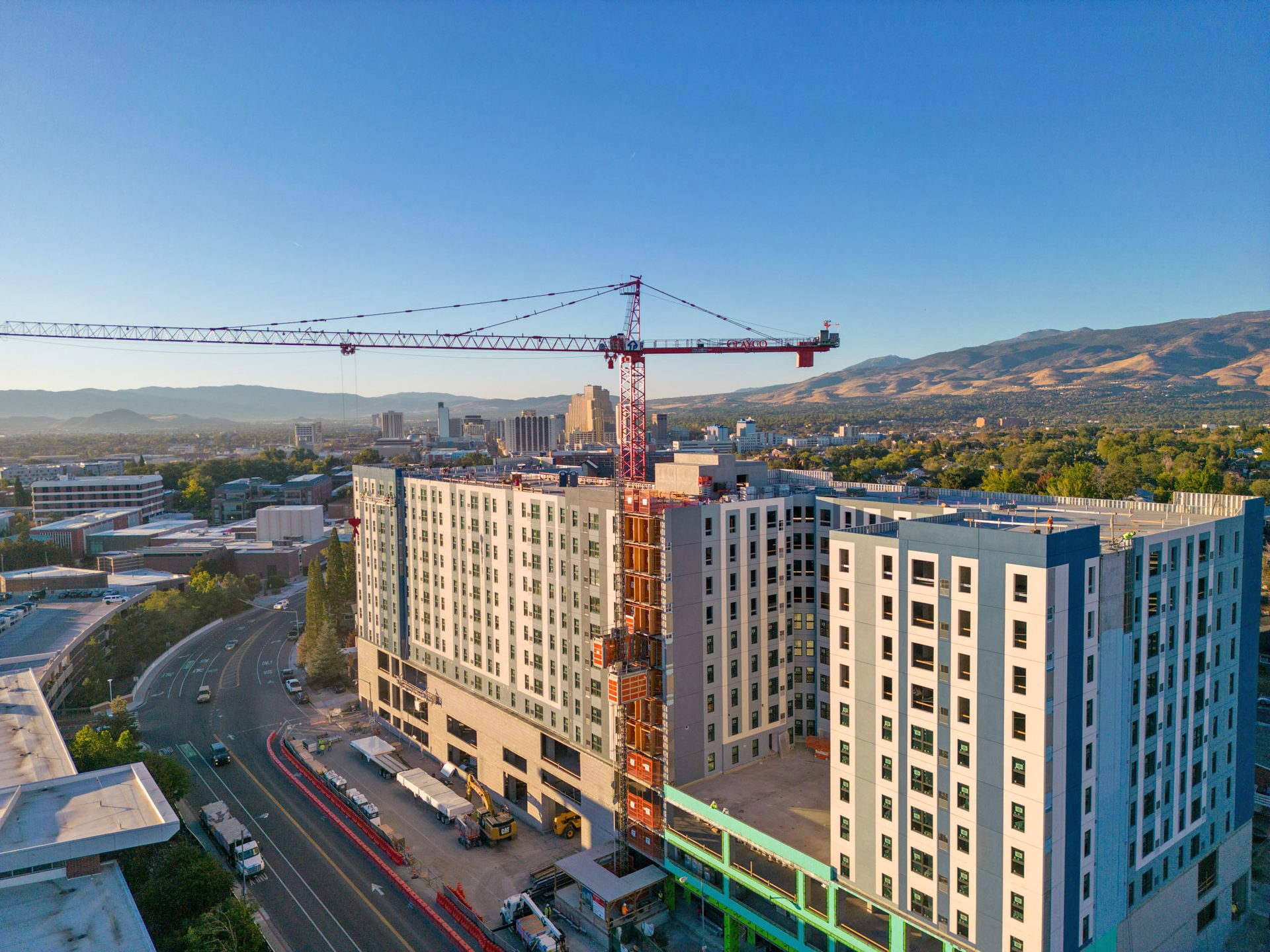 Aerial view of a multi-story building under construction with a red crane, city, and mountains.
