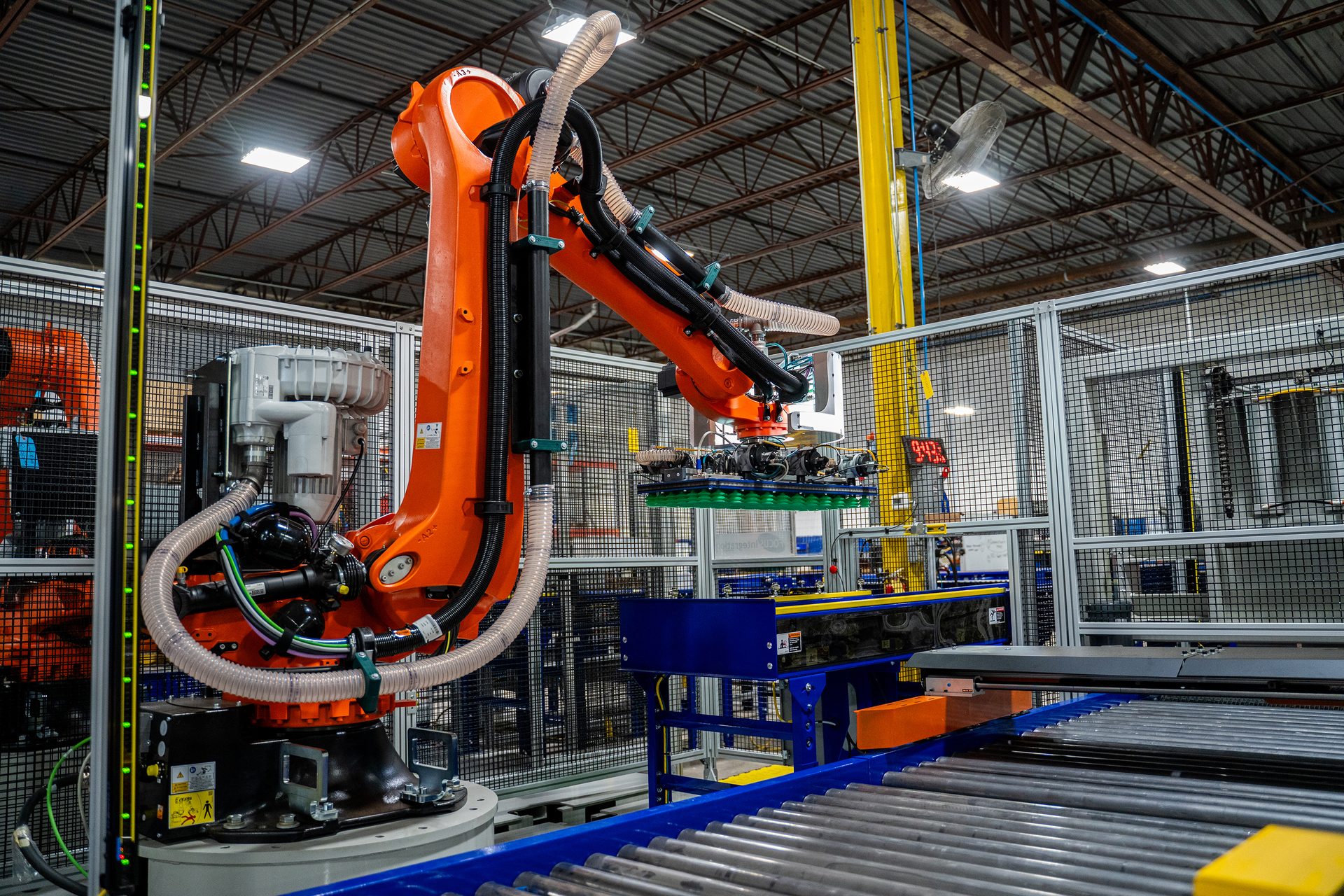 An orange robotic arm moves electronics onto a conveyor belt in a factory setting.