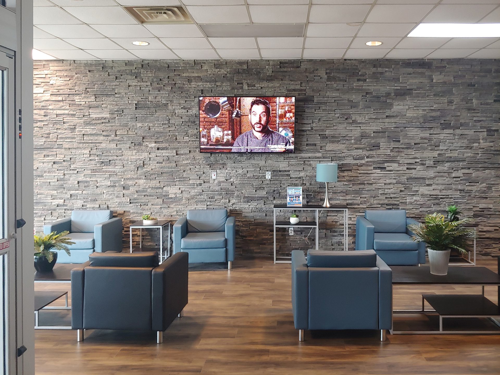 Modern waiting room with a stone accent wall, TV, and blue/black armchairs with tables.