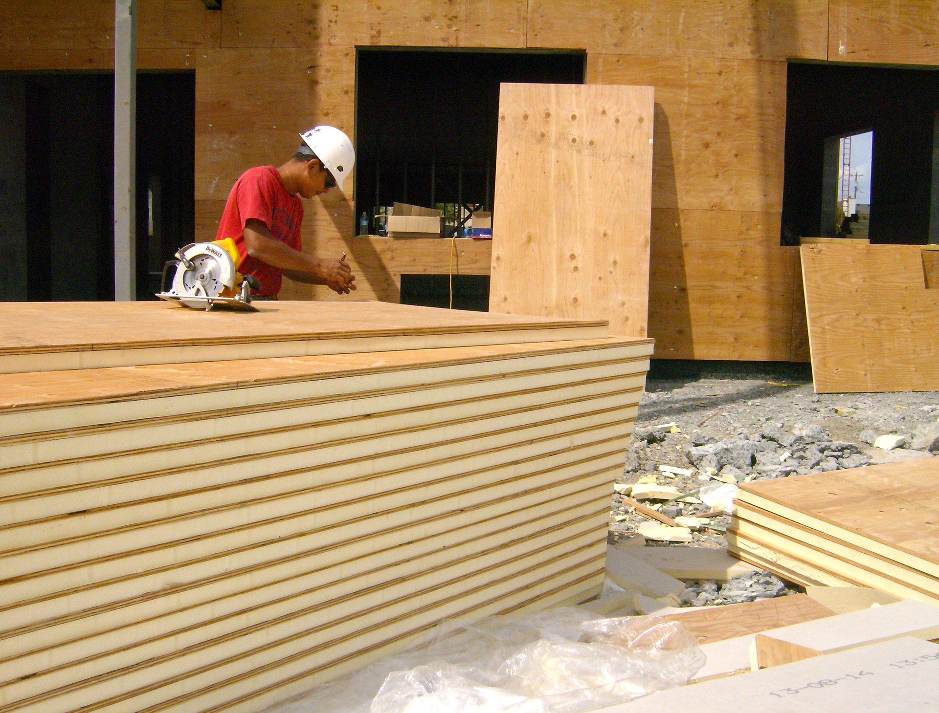 A worker at a construction site with a circular saw on plywood panels, preparing to cut.