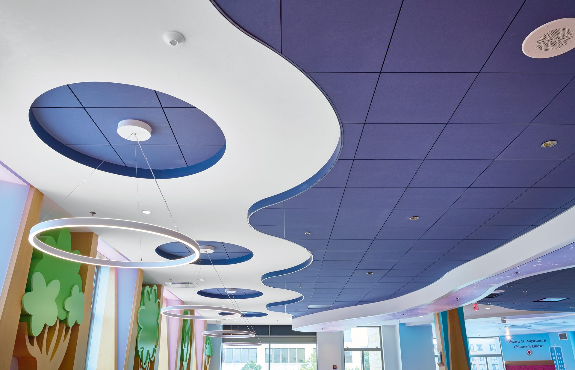 Modern ceiling featuring wavy white and blue panels, a purple grid, and circular pendant lights.