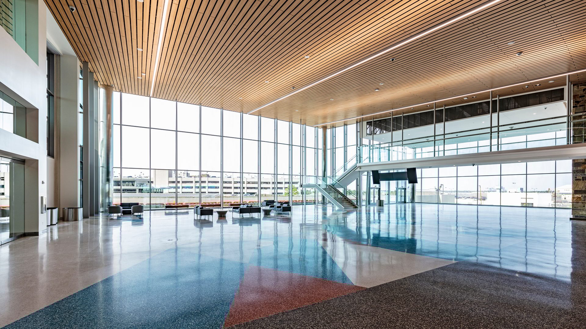 Modern airport terminal interior with high wood-slat ceiling, large windows, polished floor, and seating.