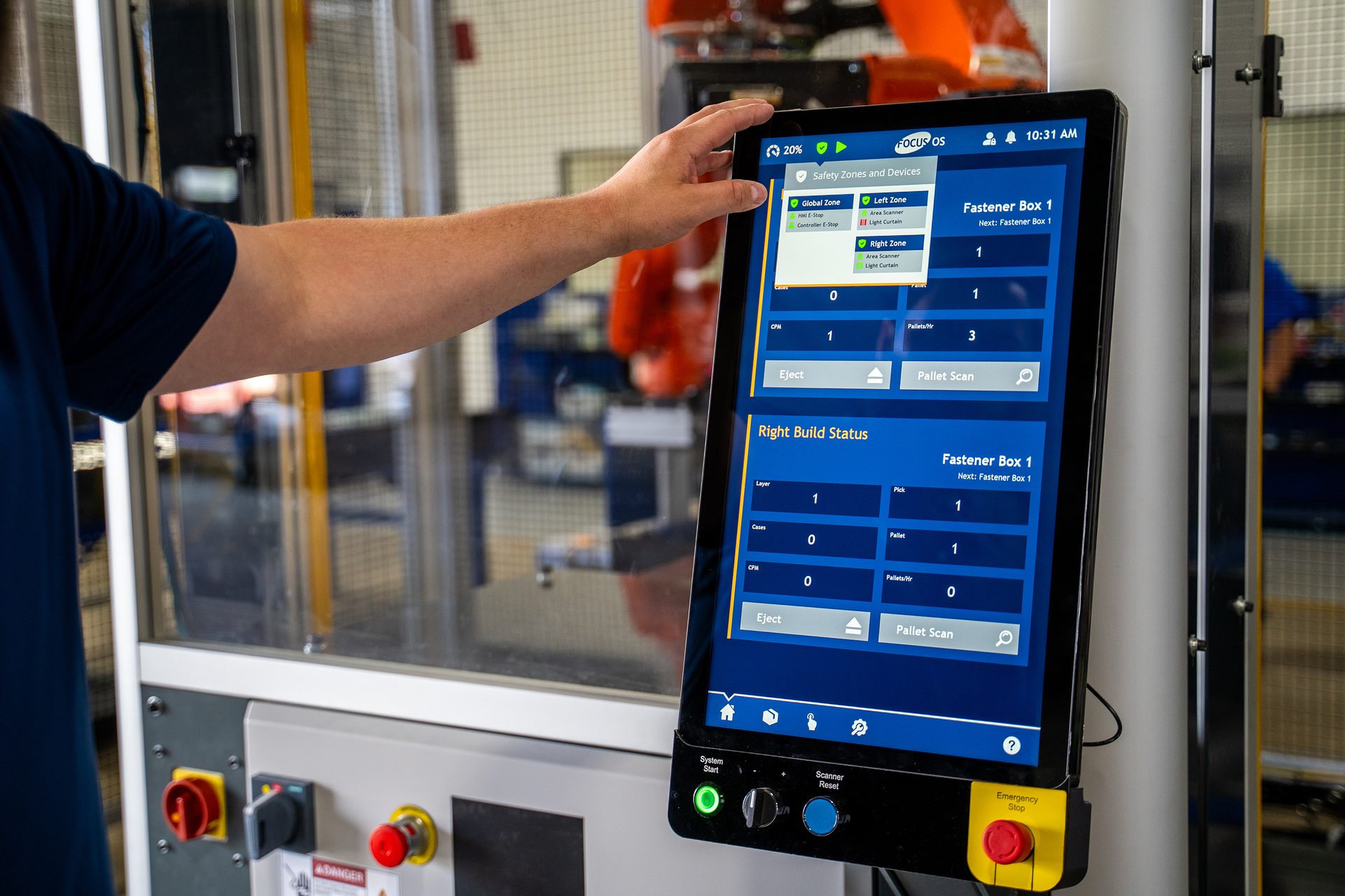 A person's hand interacts with a factory touchscreen displaying industrial data and safety features.