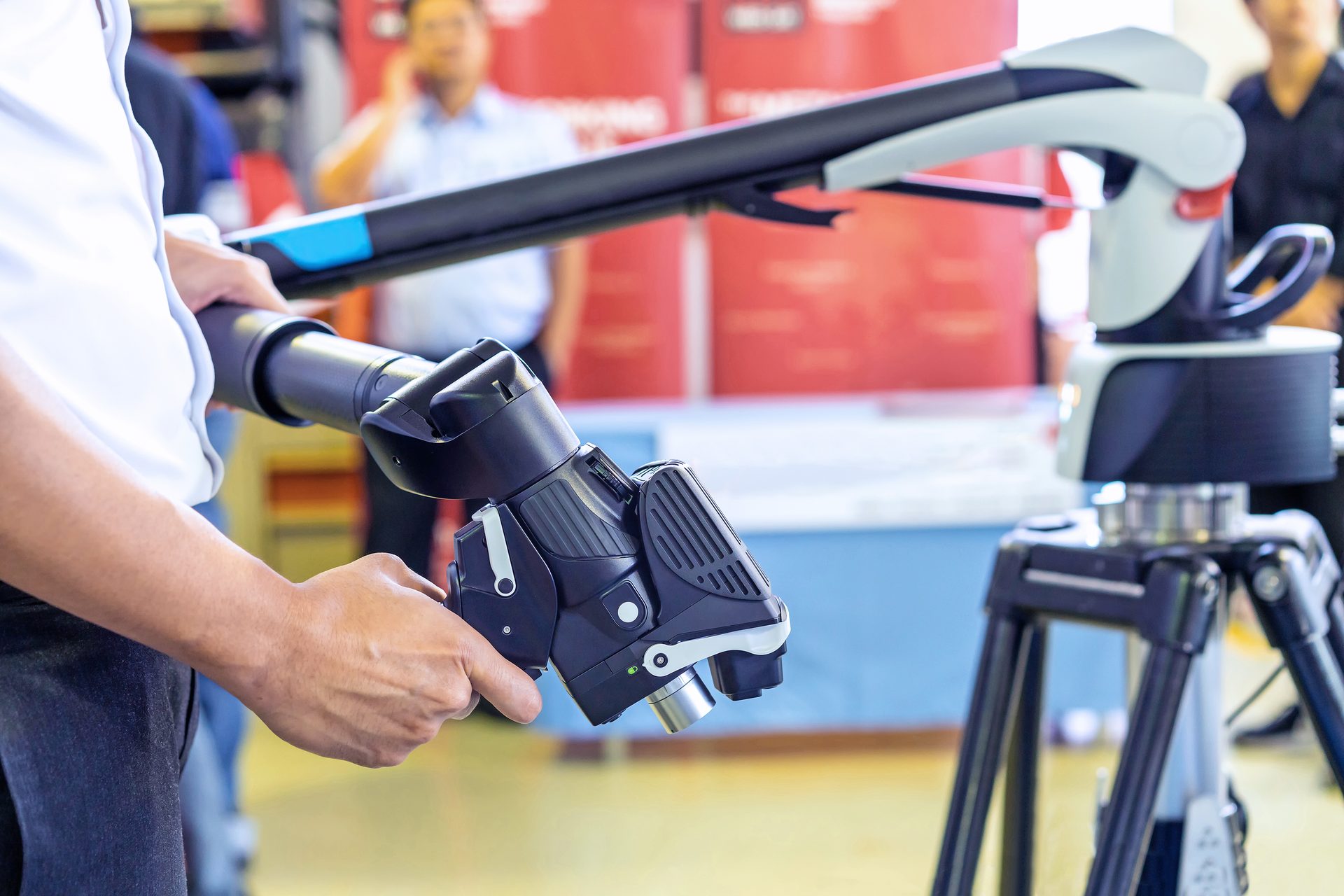 Person operating a portable 3D scanner or CMM arm, with the device's base on a tripod.