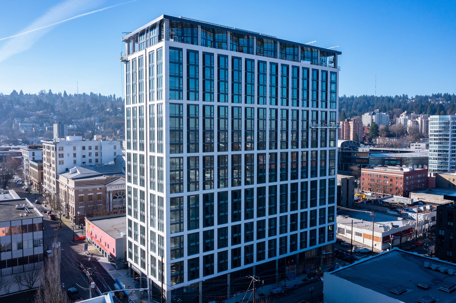 Tall modern building with a gridded window facade in a city, with hills in the distance.