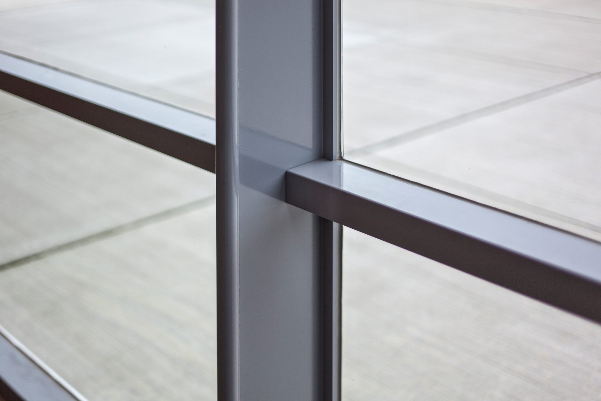 Gray metal window frame intersection with blurred light background seen through glass.