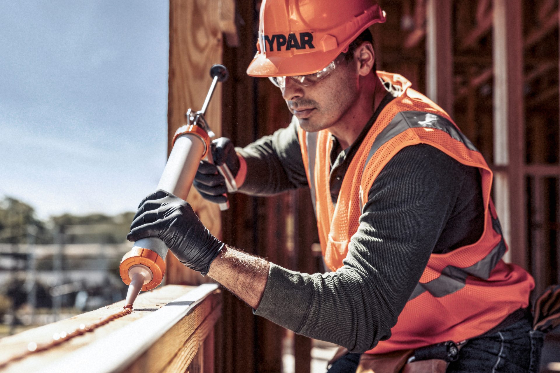 Construction worker in hard hat and safety vest applying caulk with a caulk gun.