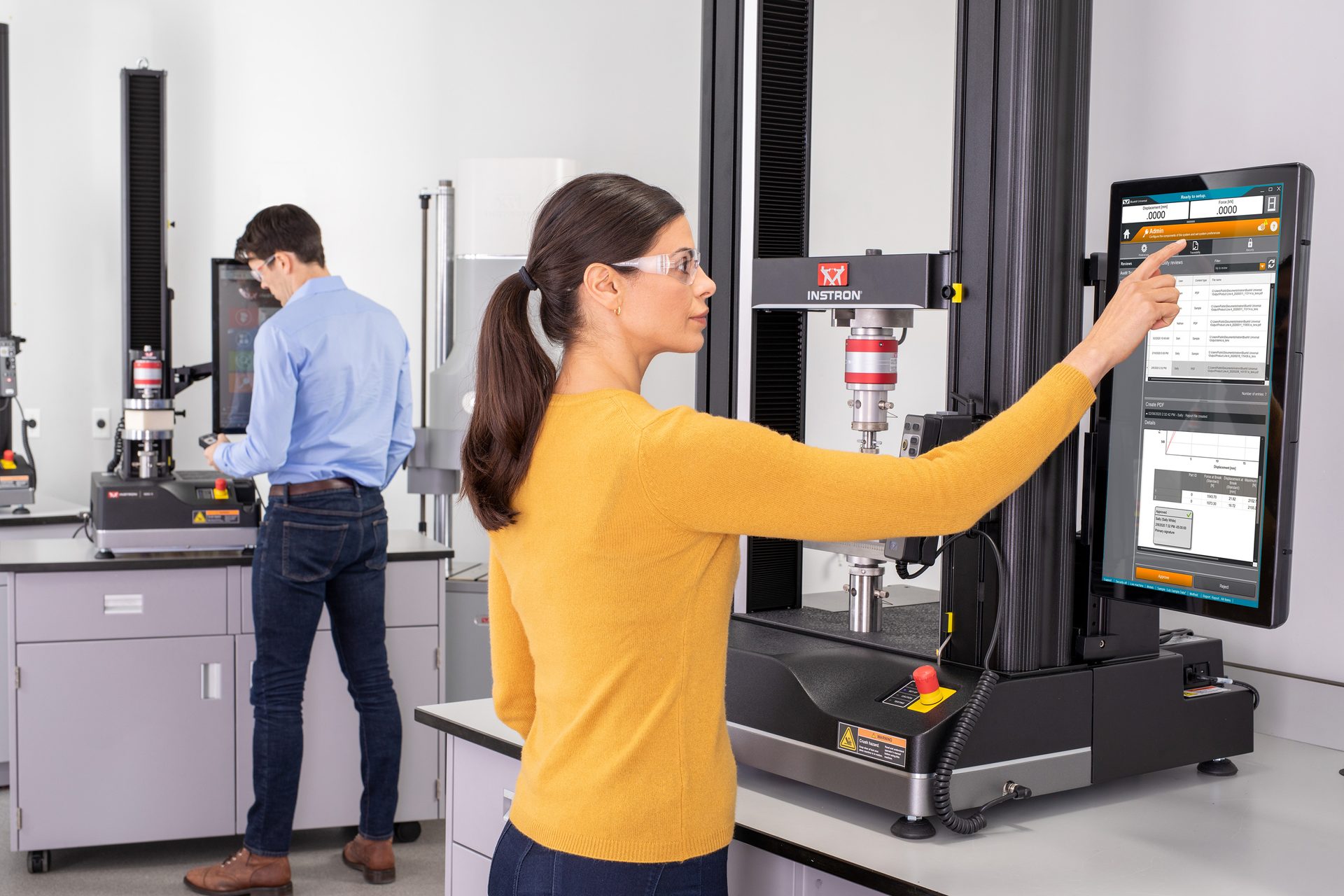 Woman in lab uses Instron material testing machine, while man operates another in the background.