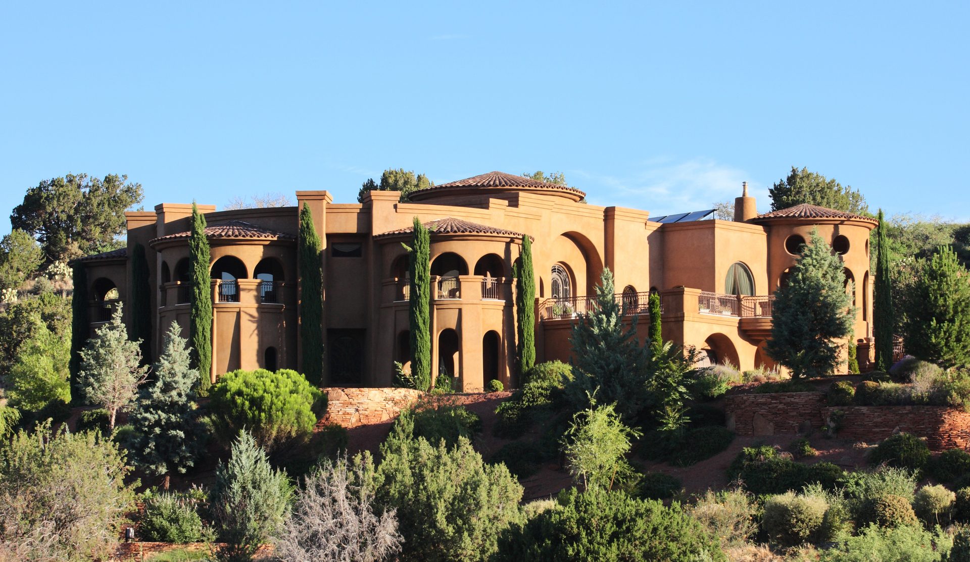 Luxury mansion built into the side of a hill with beautifully manicured desert landscape yard under a sunrise sky. Pine Valley - Sedona, Arizona,