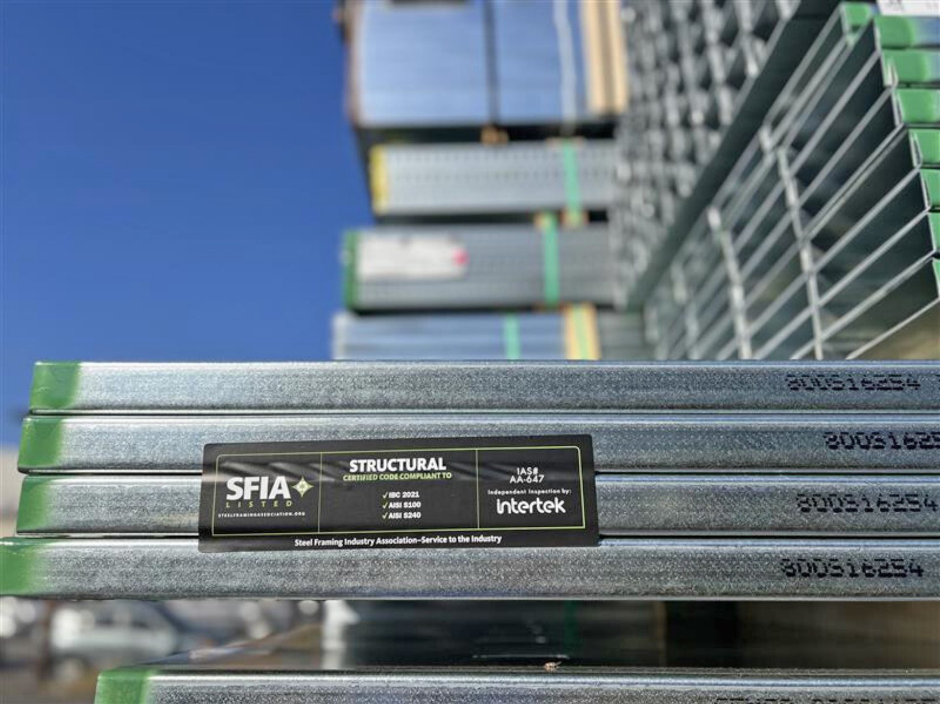 Close-up of galvanized steel studs stacked with an SFIA Certified Code Compliant label visible on one stud, showing quality assurance.