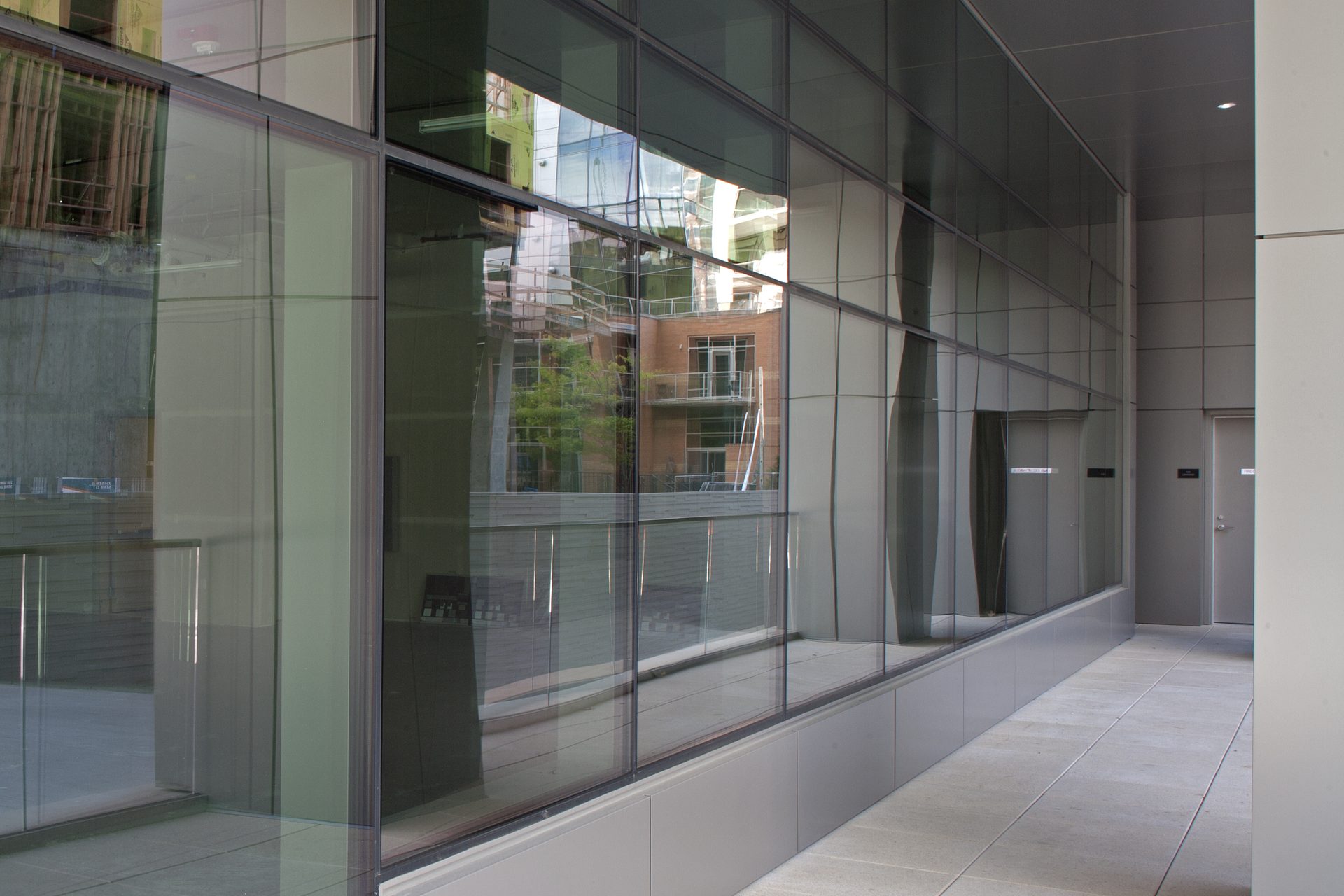 Glass facade of a modern building reflecting a brick building and trees, with a walkway.