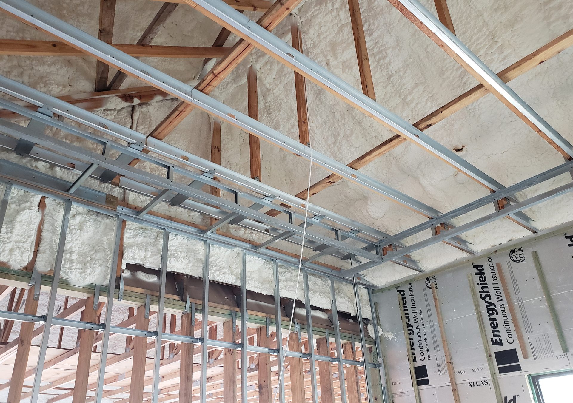 Interior view of a building under construction featuring spray foam insulation, metal, and wood framing.