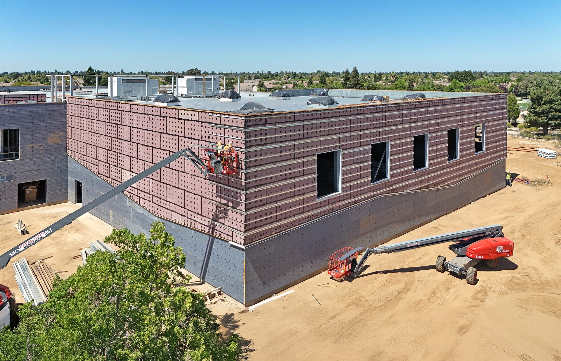 Workers on a boom lift install exterior panels on a large building under construction.