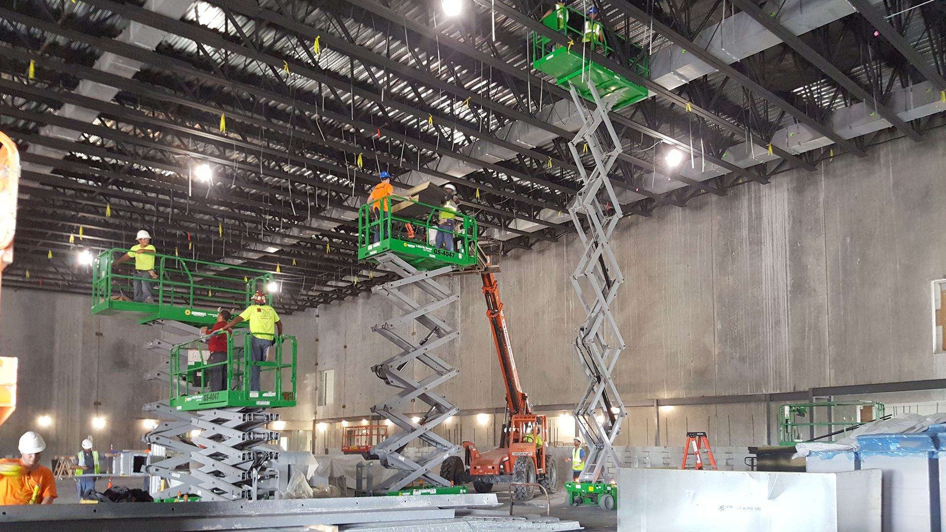 Construction workers on scissor lifts install ceiling components in a large commercial building.