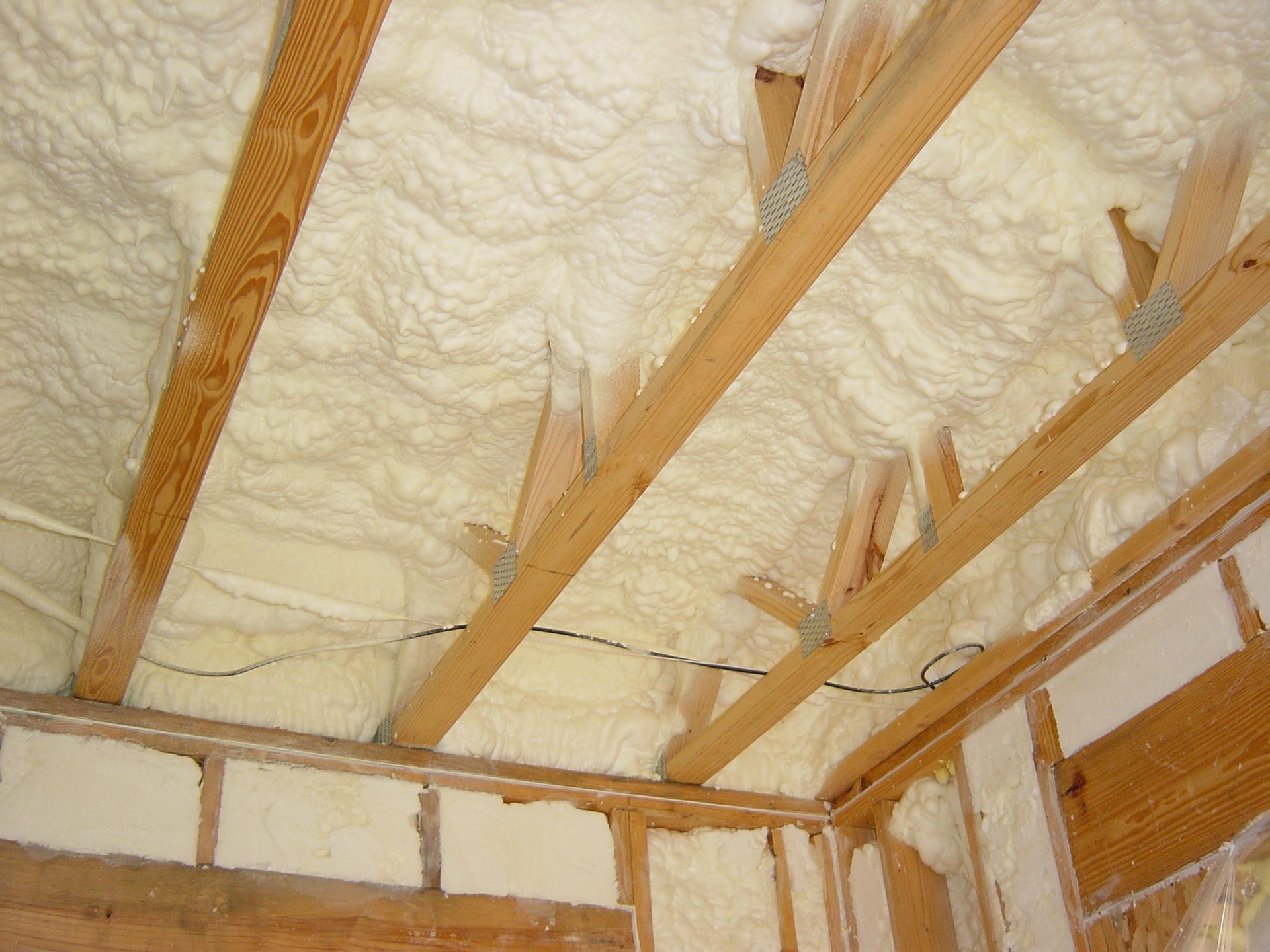 Spray foam insulation covering ceiling and wall framing in an unfinished space.