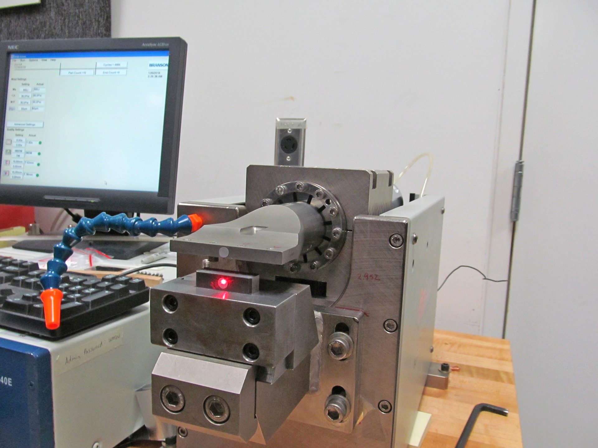 A piece of industrial equipment with a monitor, keyboard, a blue flexible hose, and a red laser dot.