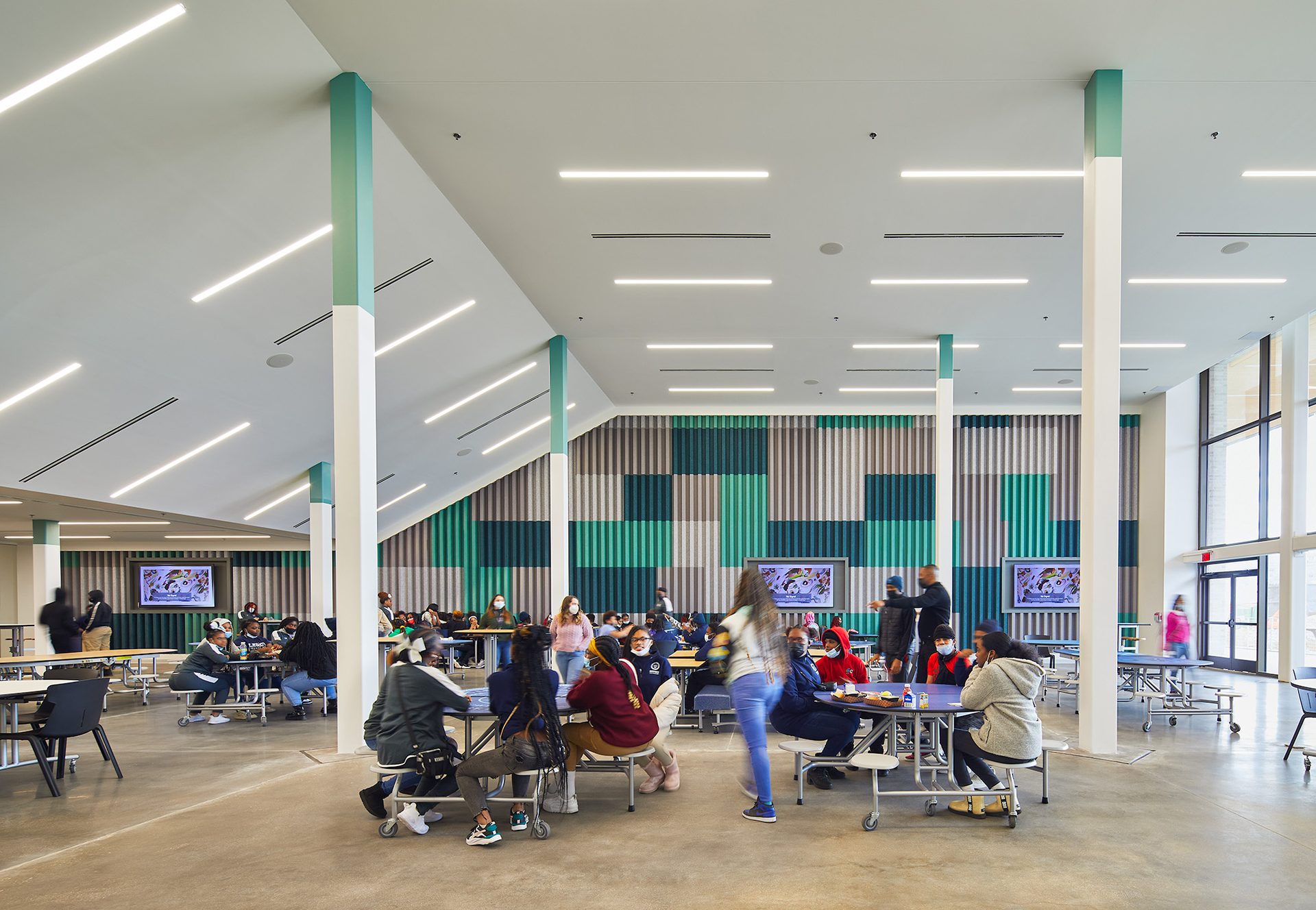 Modern cafeteria with students, patterned walls, green pillars, and geometric lighting.