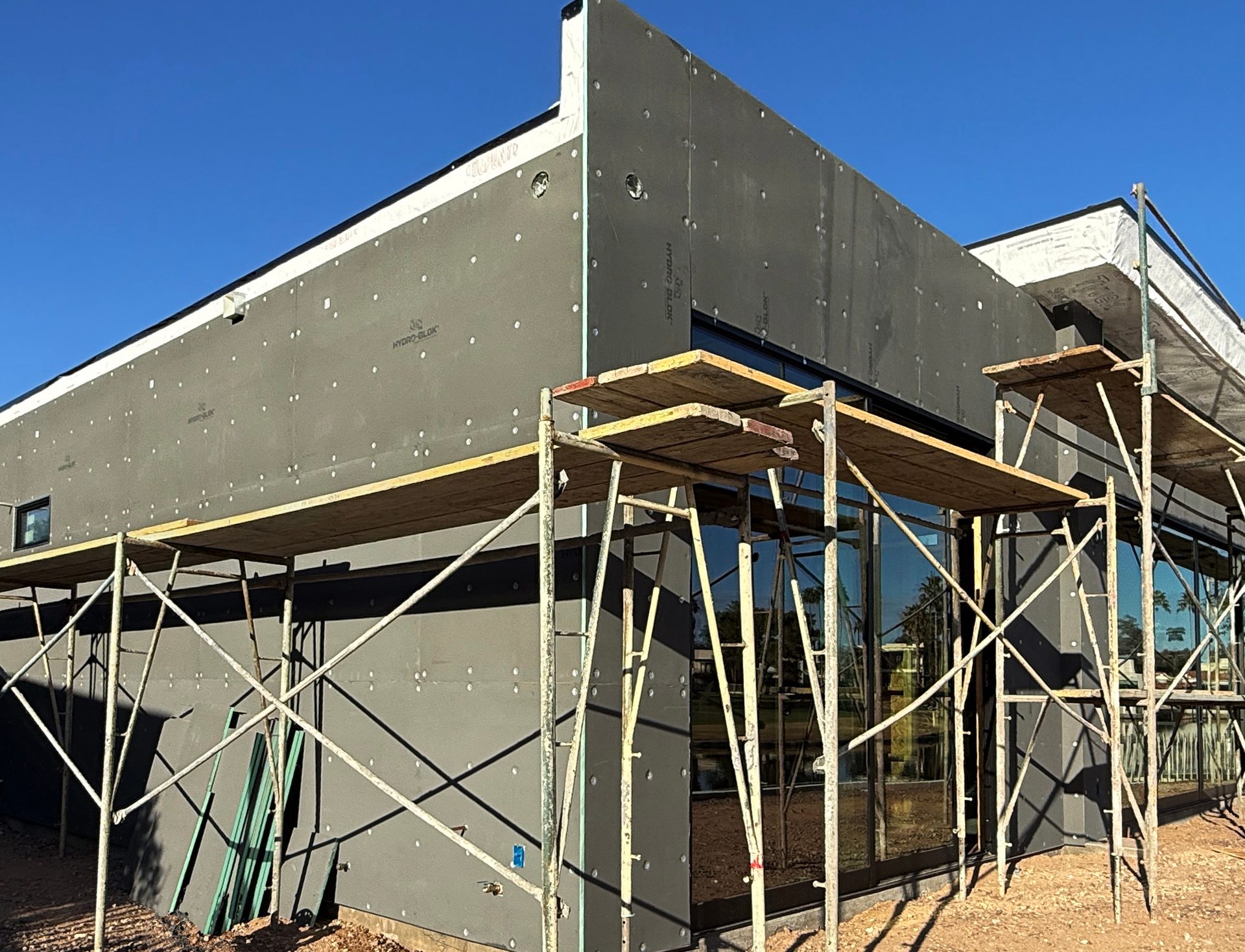 Exterior of a modern building under construction with gray sheathing and scaffolding against a blue sky.