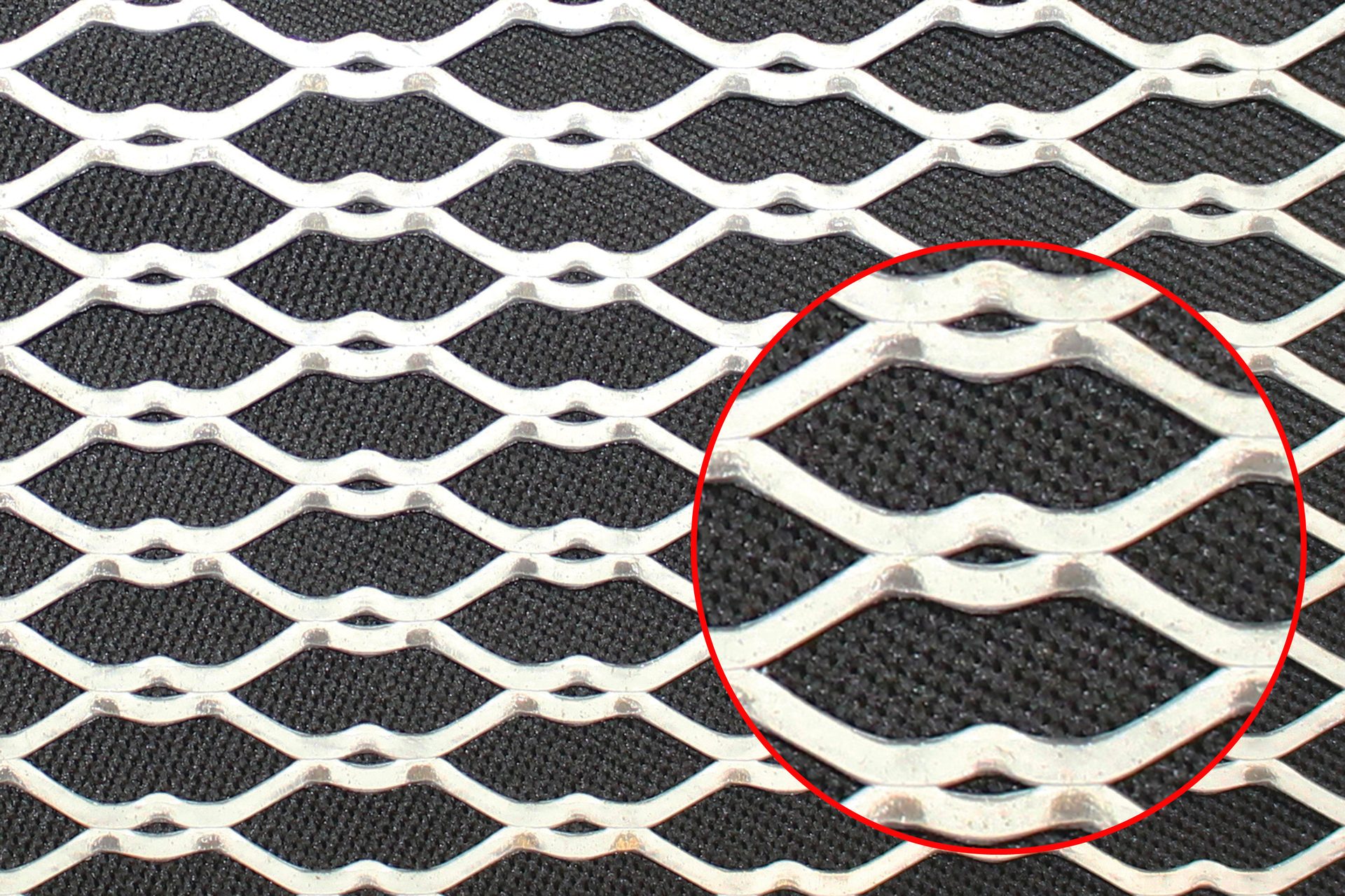 Close-up of a silver expanded metal mesh with a diamond pattern over a black textured background.