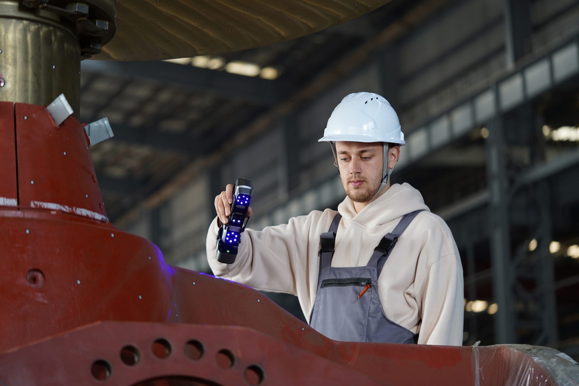 Worker in hard hat 3D scanning a large red industrial component with a handheld scanner.