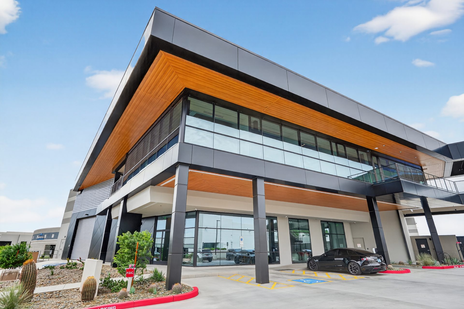Contemporary building with dark grey and wood siding, glass windows, a parked black car.