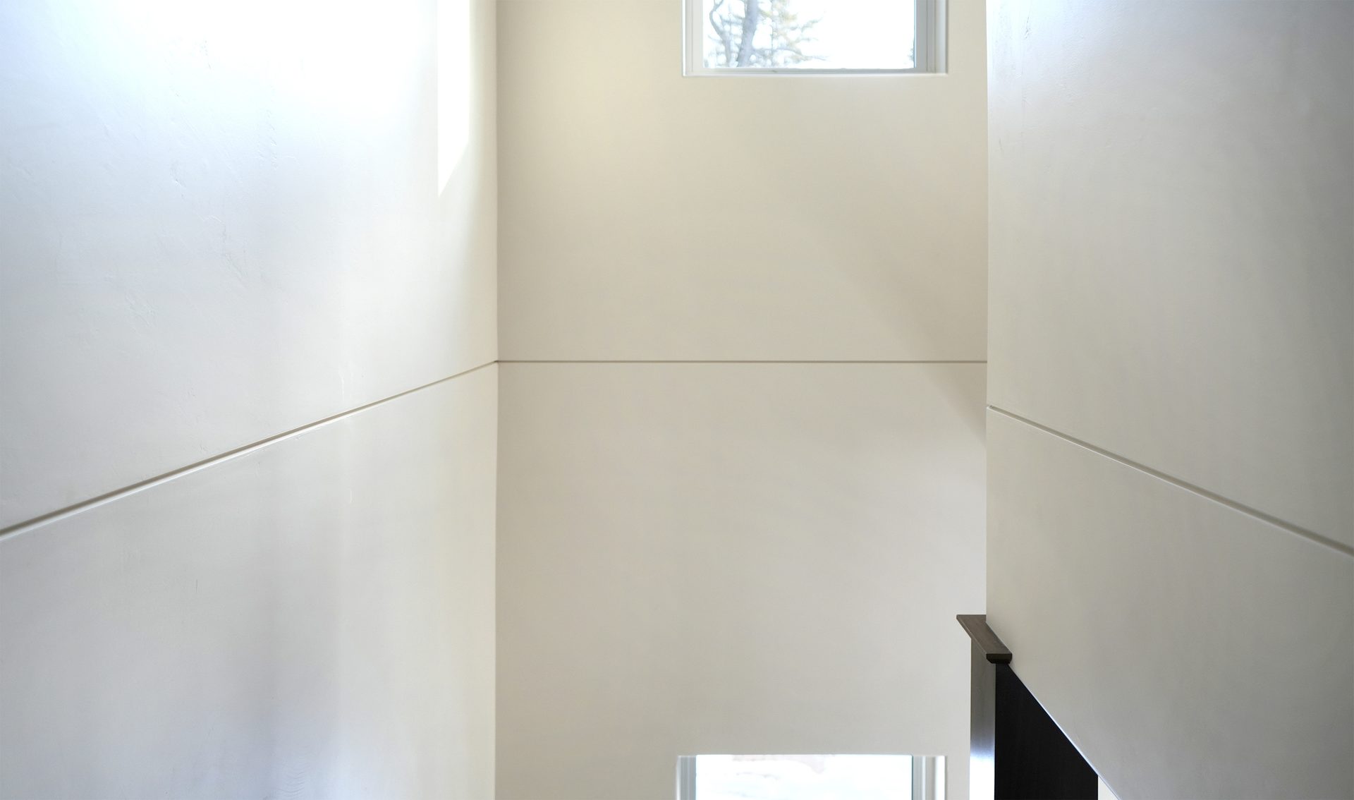 Minimalist interior with light grooved walls, windows, and a dark handrail.