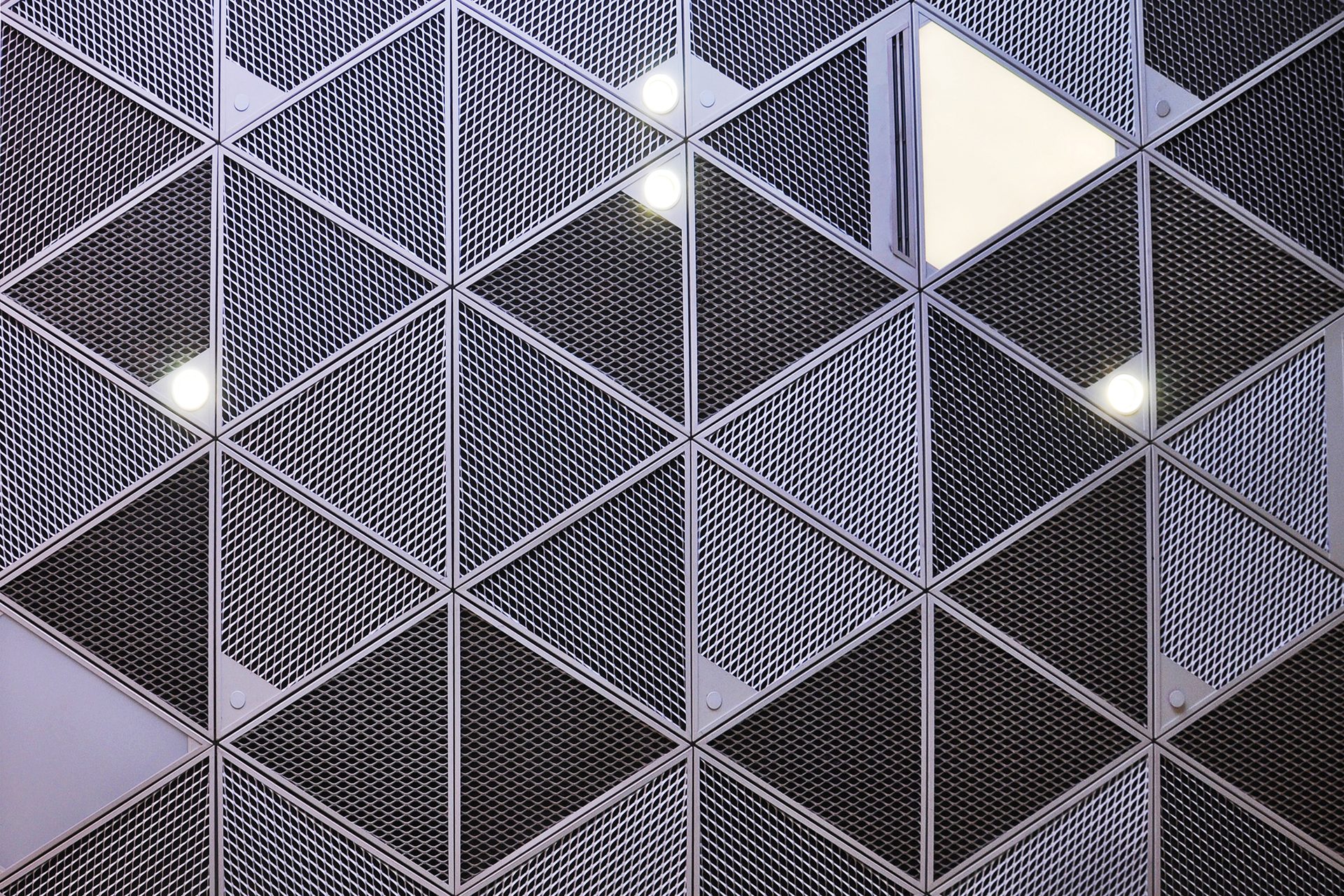 Triangular mesh panels form a geometric pattern, some featuring lights and solid sections.