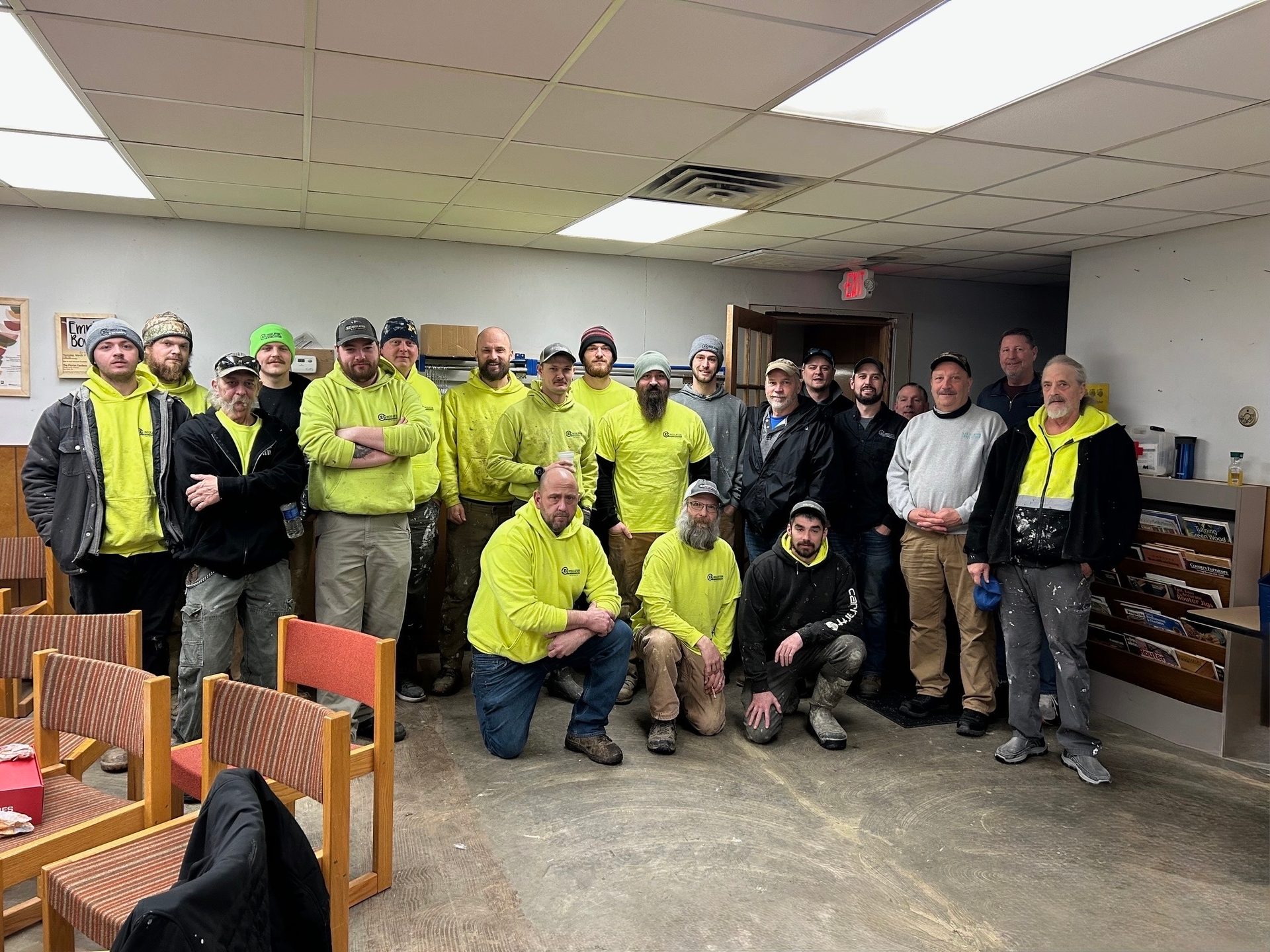 Group of male workers in yellow shirts and hats posing indoors.