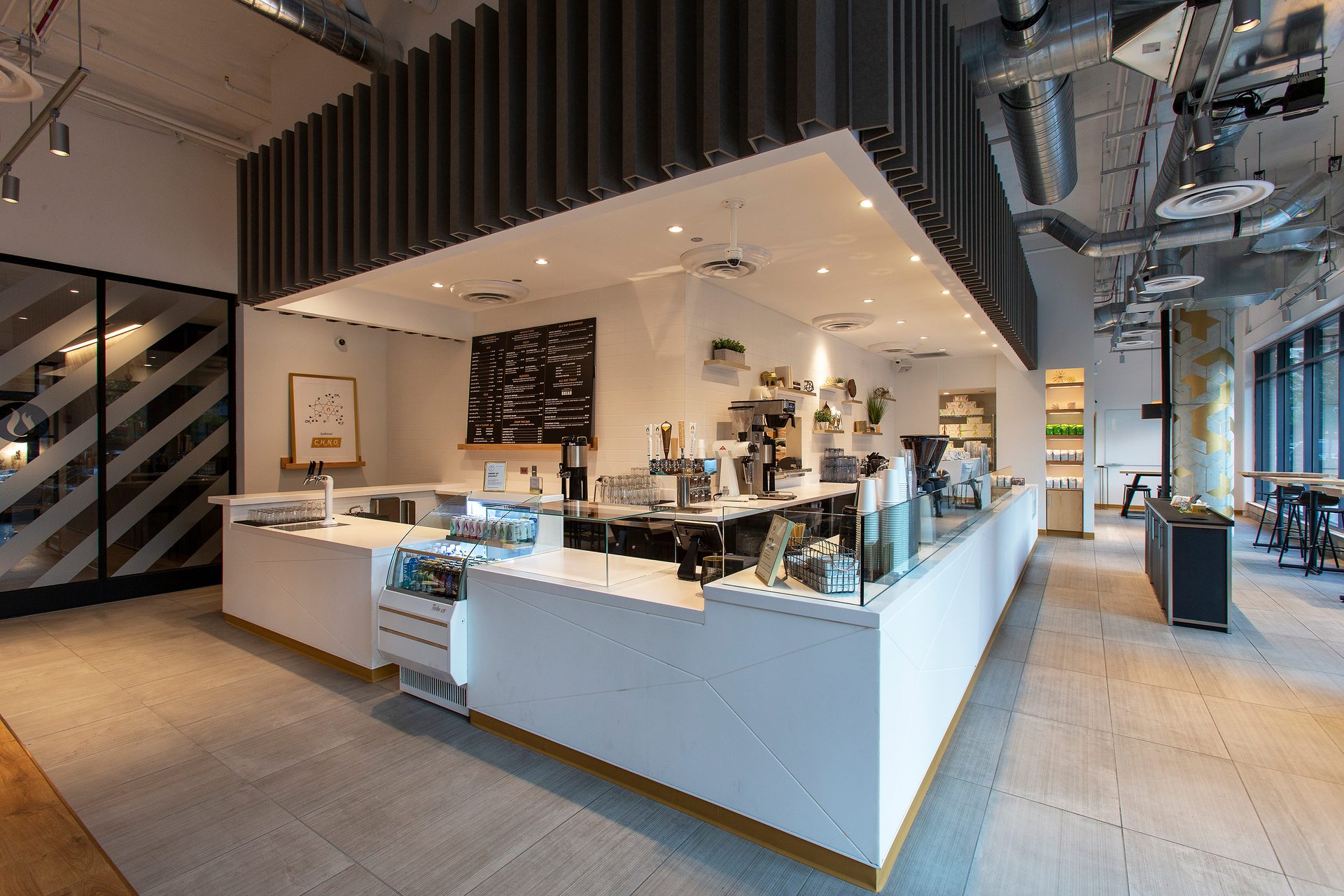 Modern coffee shop interior with a long white counter, menu, and industrial ceiling.