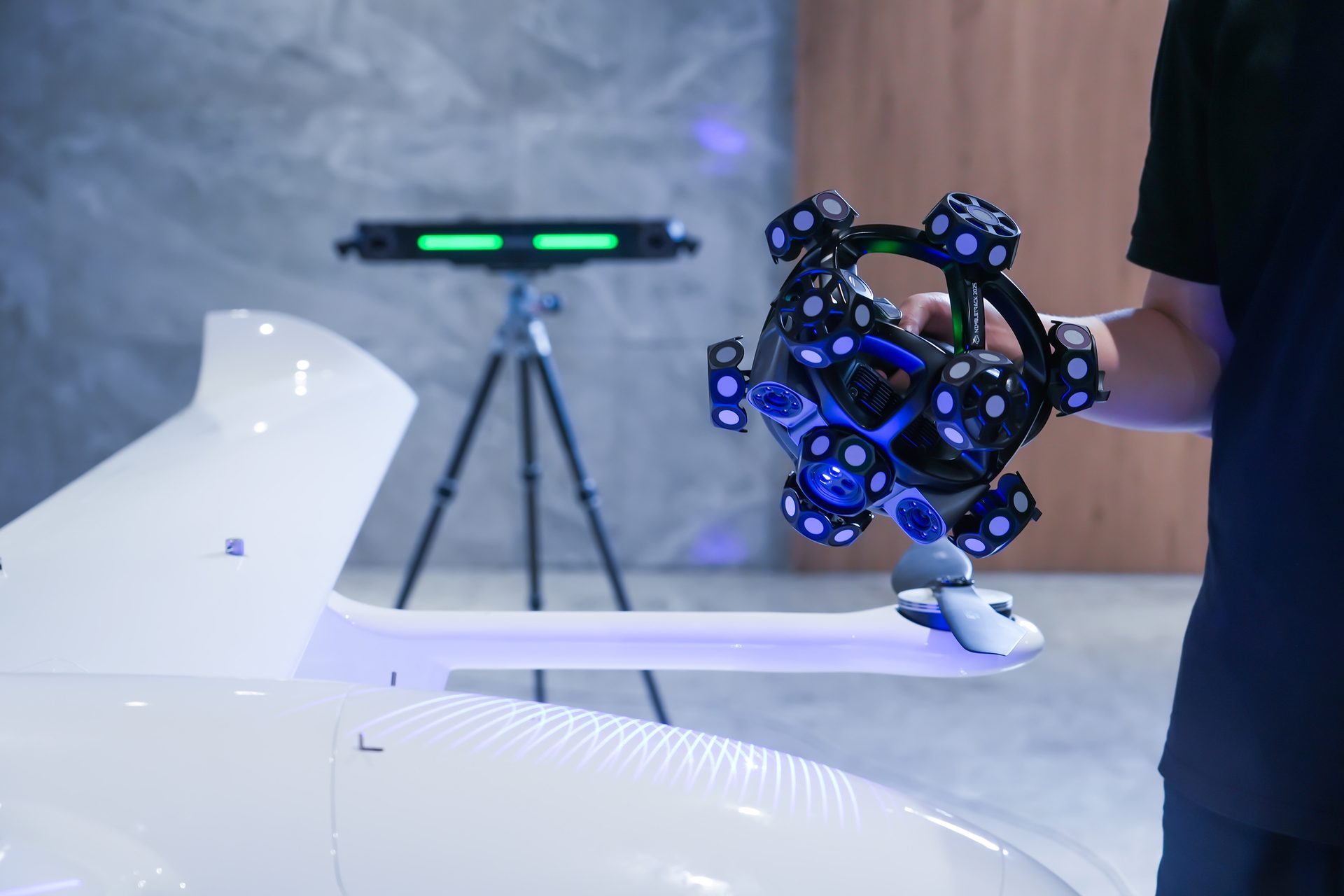 Handheld 3D scanner used on a white drone/aircraft part, with a green tracking system.