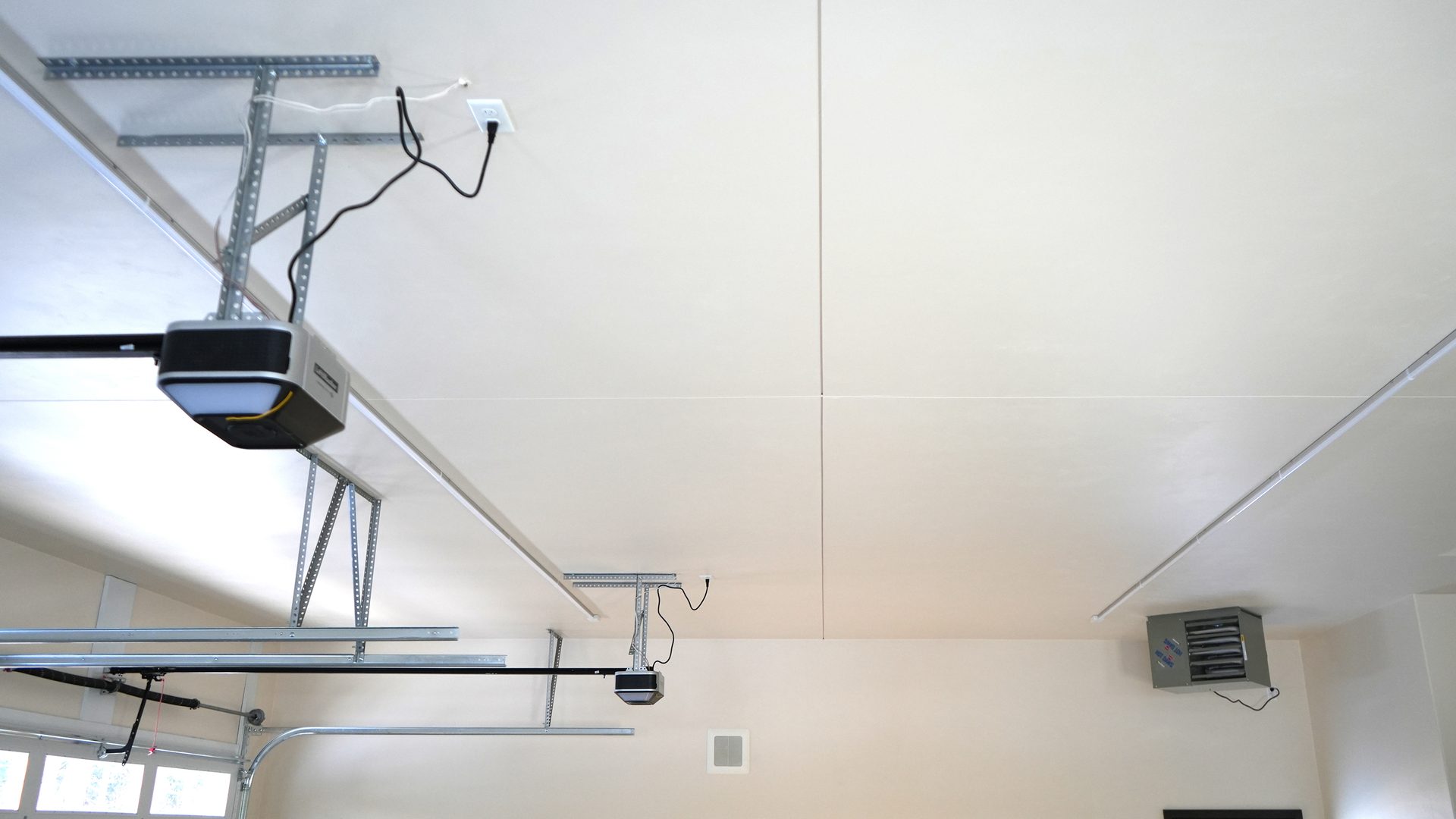 Clean white garage ceiling with two garage door openers, metal supports, and a ceiling-mounted heater.