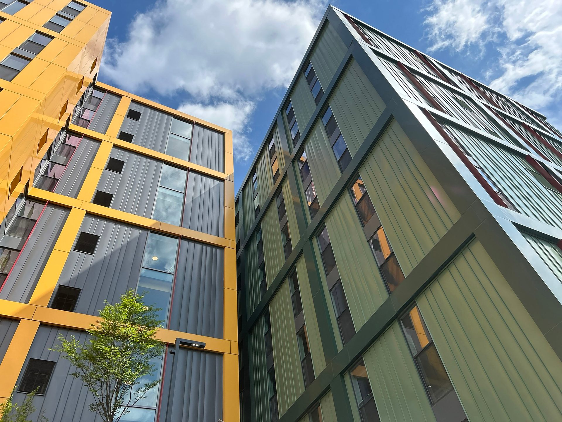 Modern yellow and green buildings against a cloudy blue sky.