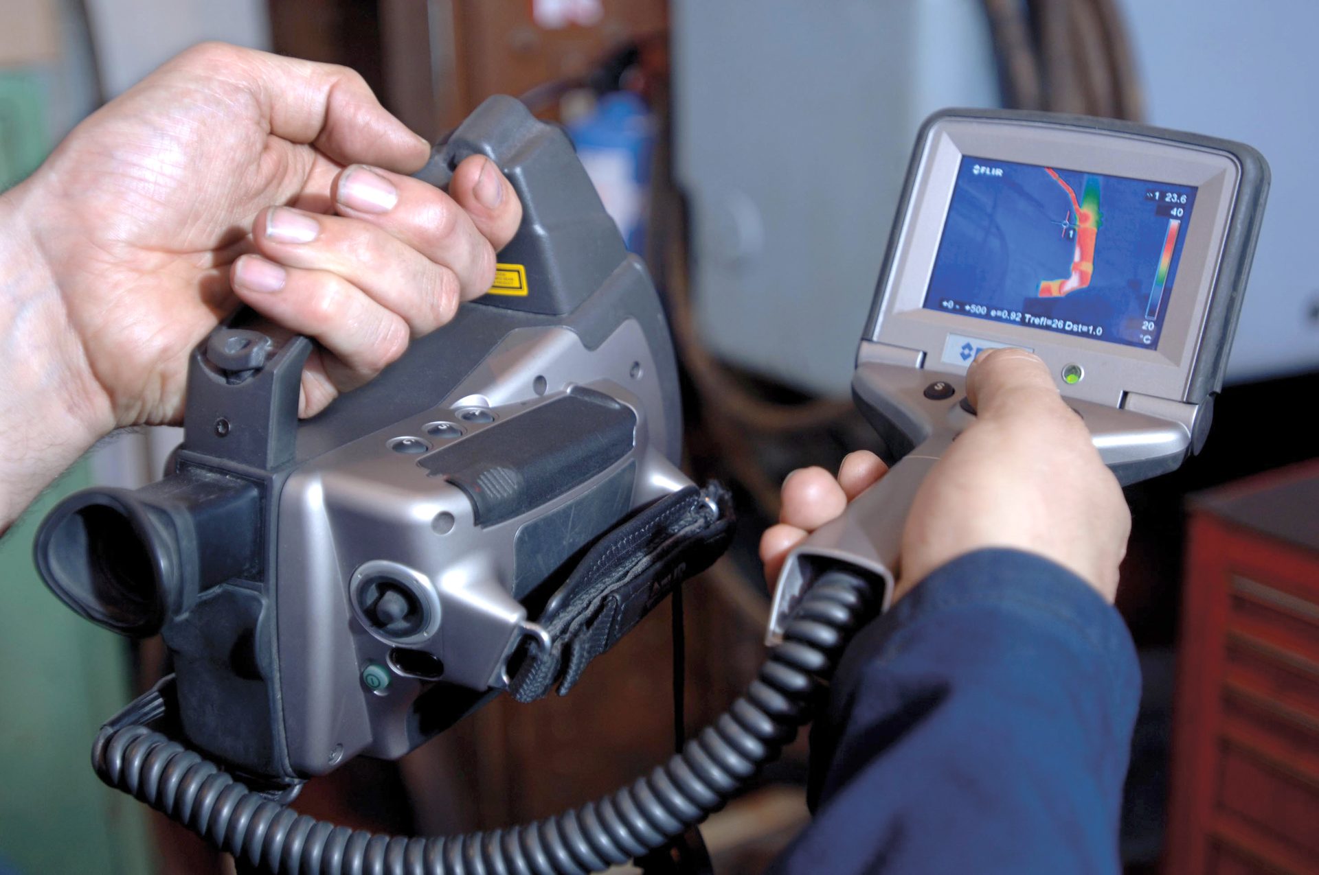 Hands operating two thermal imaging cameras, one displaying temperature on its screen.
