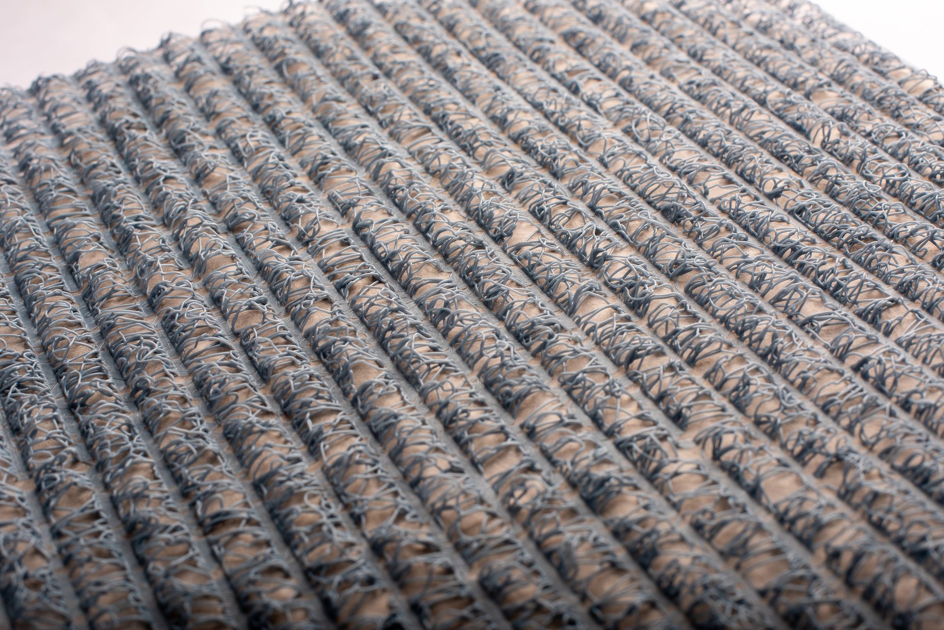 Close-up of a grey tangled looped mat in parallel rows on a light background.