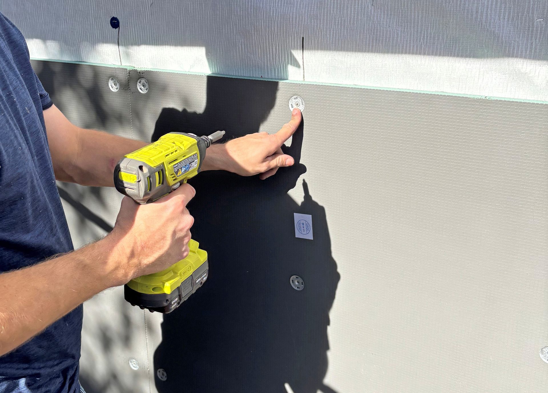 Person using a drill to install a fastener on exterior wall insulation.