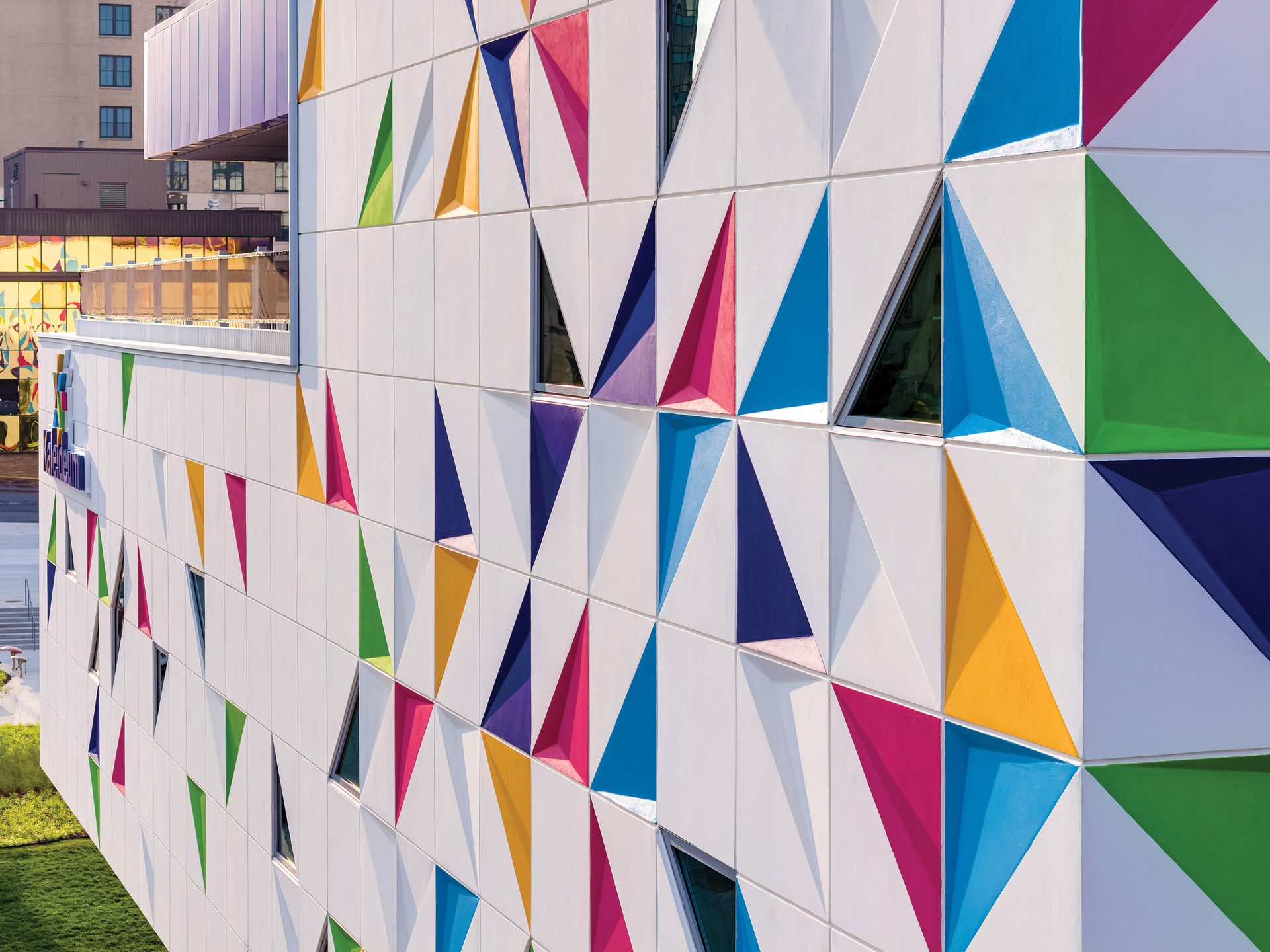 Modern building facade with a colorful geometric pattern of triangular panels in blue, green, yellow, and pink.