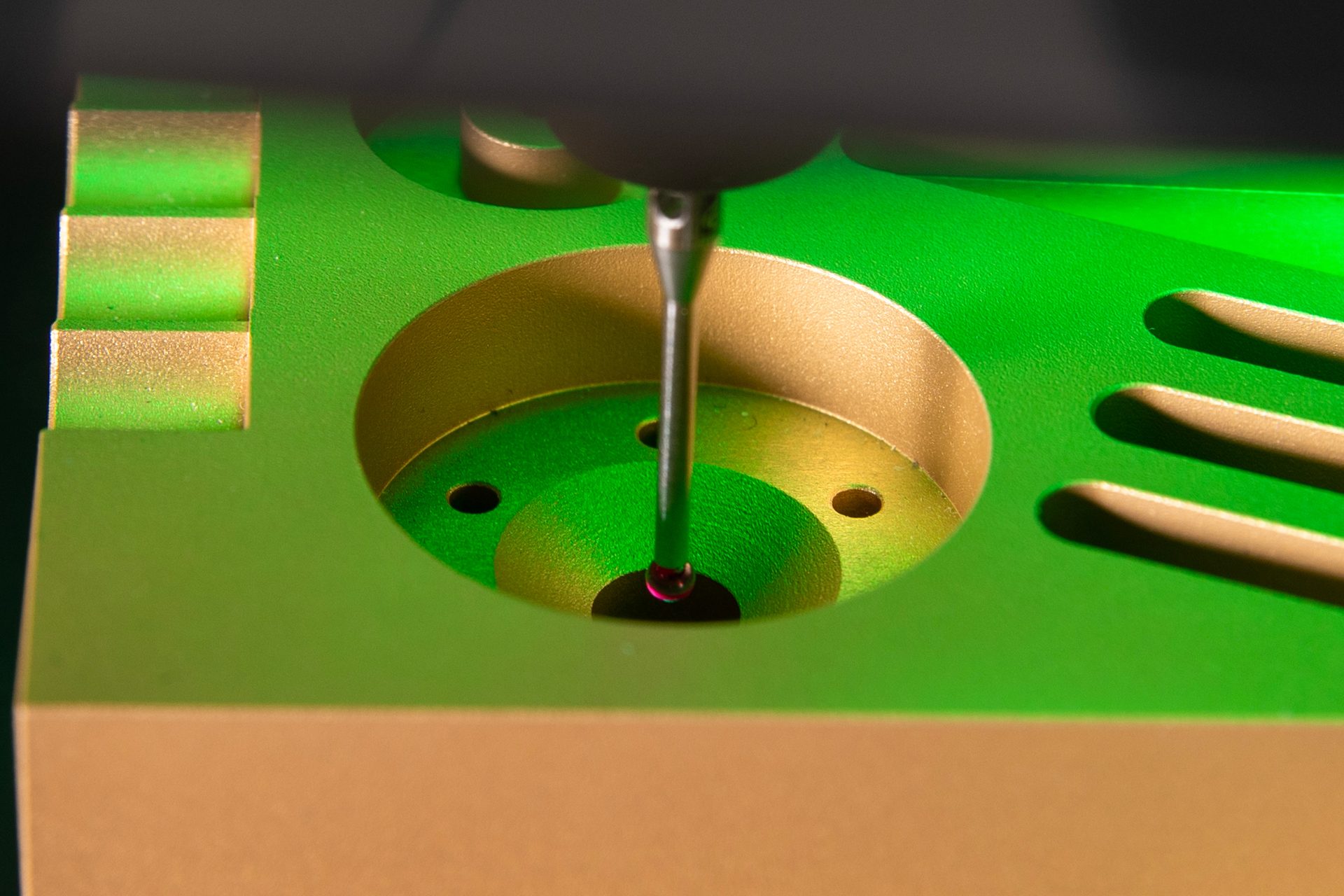CMM probe with red tip measuring a green and gold machined part.
