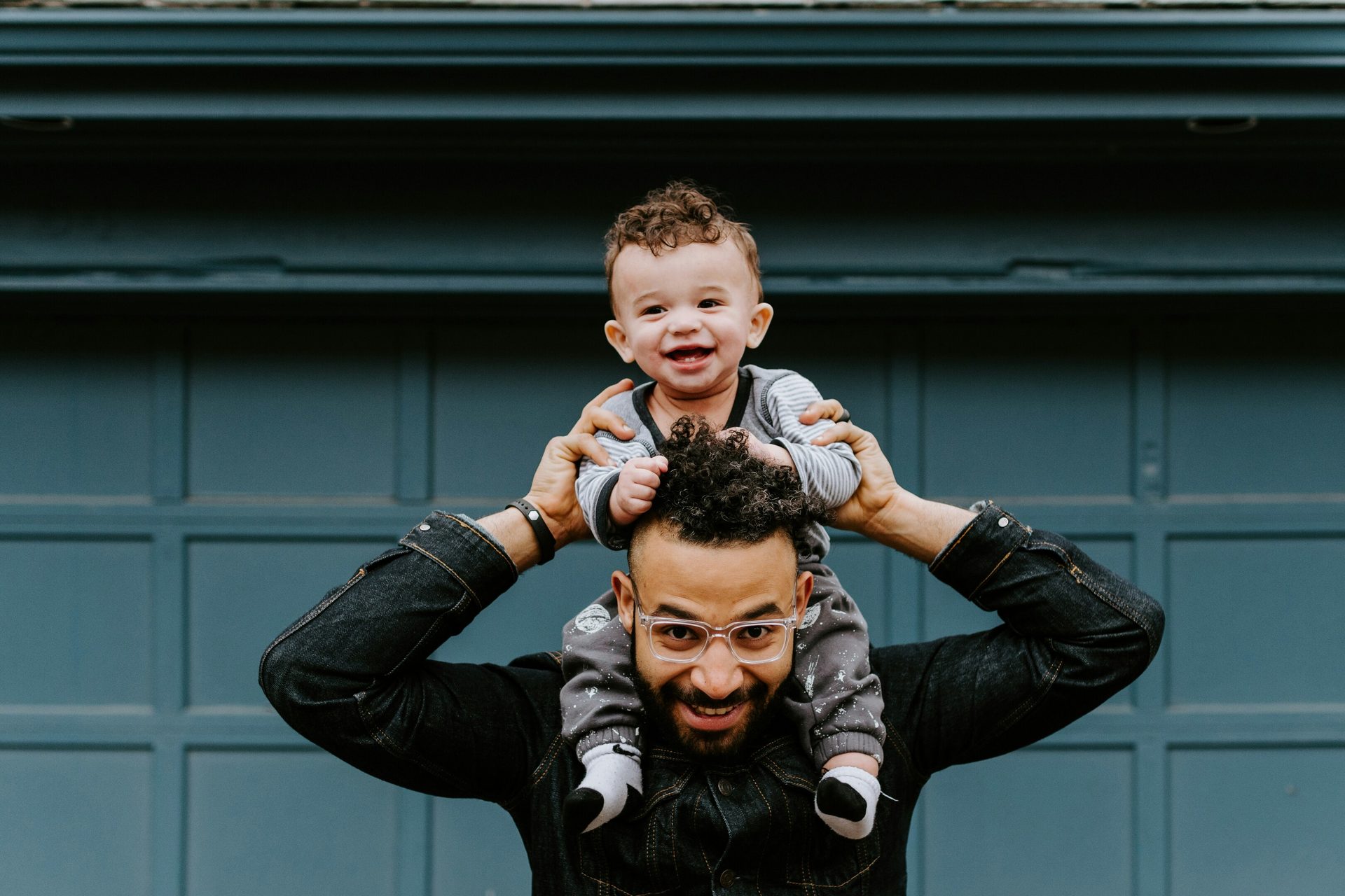 Happy father with baby on shoulders, both smiling, against a blue background.