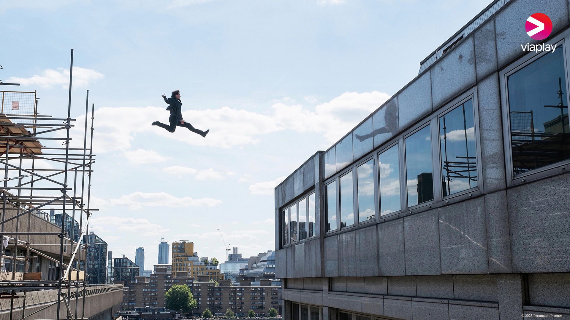 Man jumps mid-air from scaffolding to a building, with a city skyline.