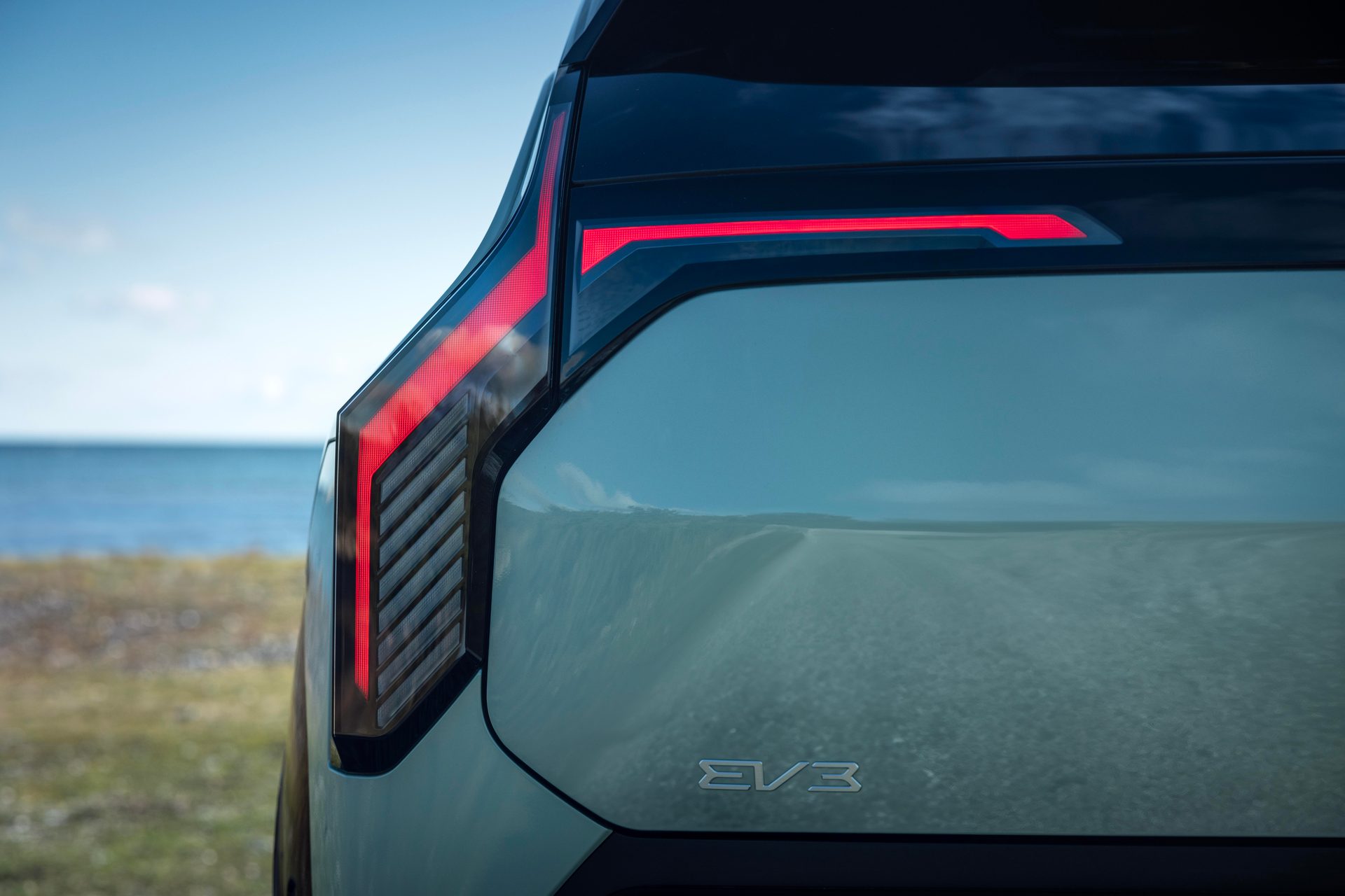 Rear of a light green EV3 car, unique red LED taillights and EV3 badge, ocean backdrop.