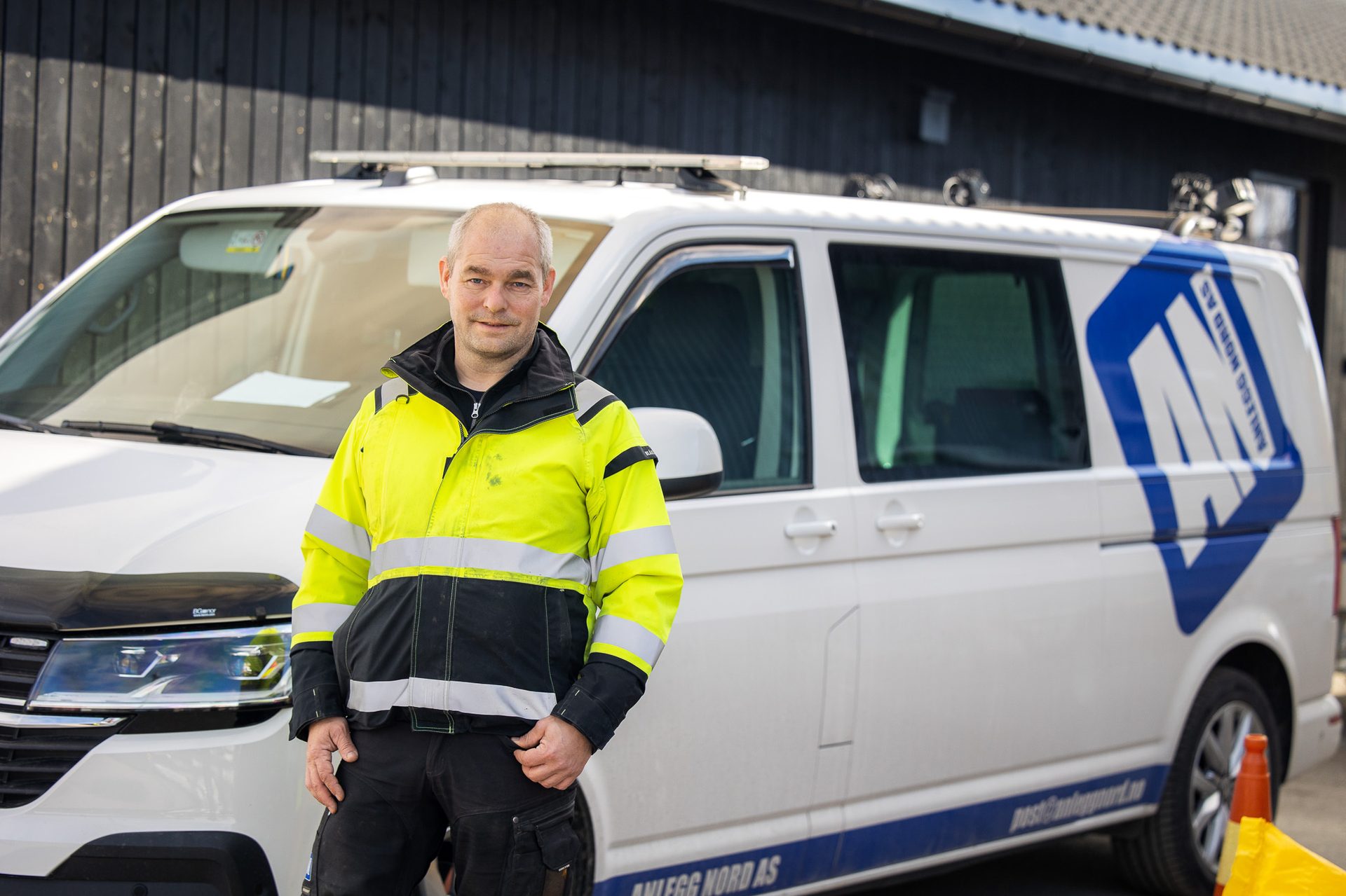 A worker in a high-visibility jacket stands next to a white company van with a blue logo.