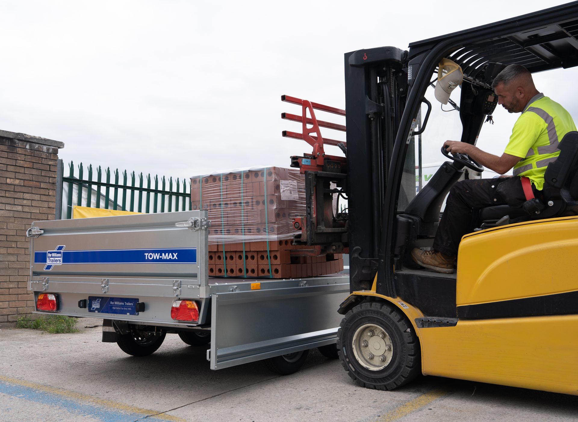 Forklift loading pallets of bricks onto a silver Ifor Williams Tow-Max trailer.