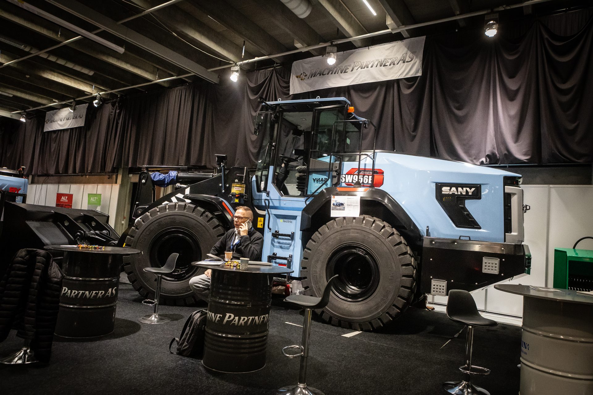 Light blue SANY wheel loader and man on phone at an indoor exhibition.