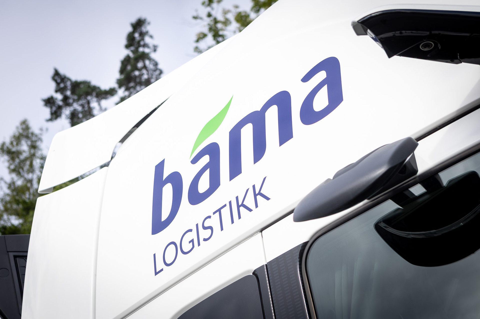 Close-up of the Bama Logistikk logo, a blue text with a green leaf, on the white side of a truck.
