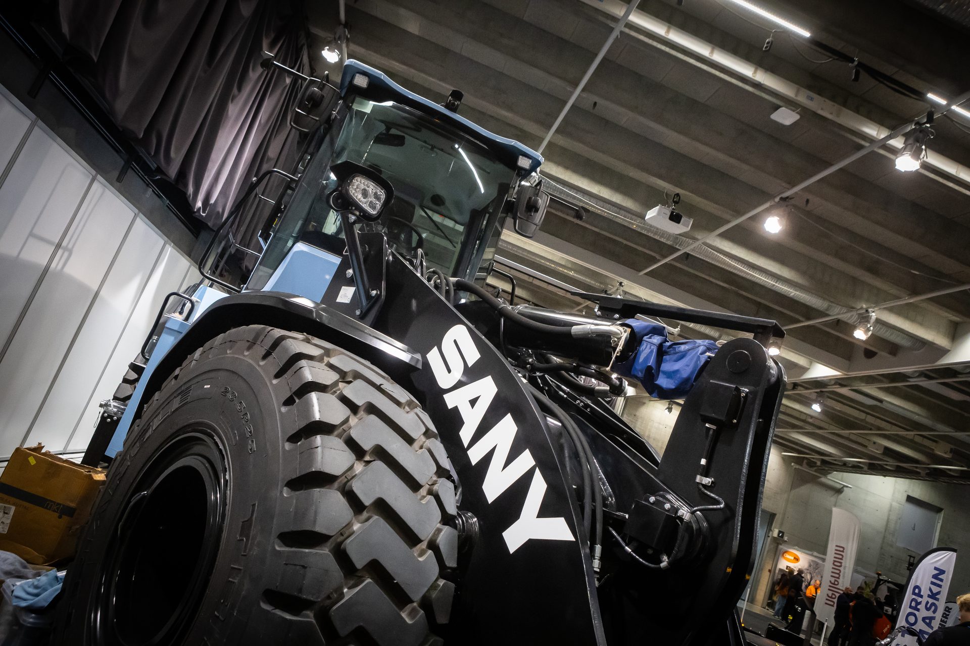 A low-angle view of a black SANY heavy machinery vehicle, showing its large tire and cabin.