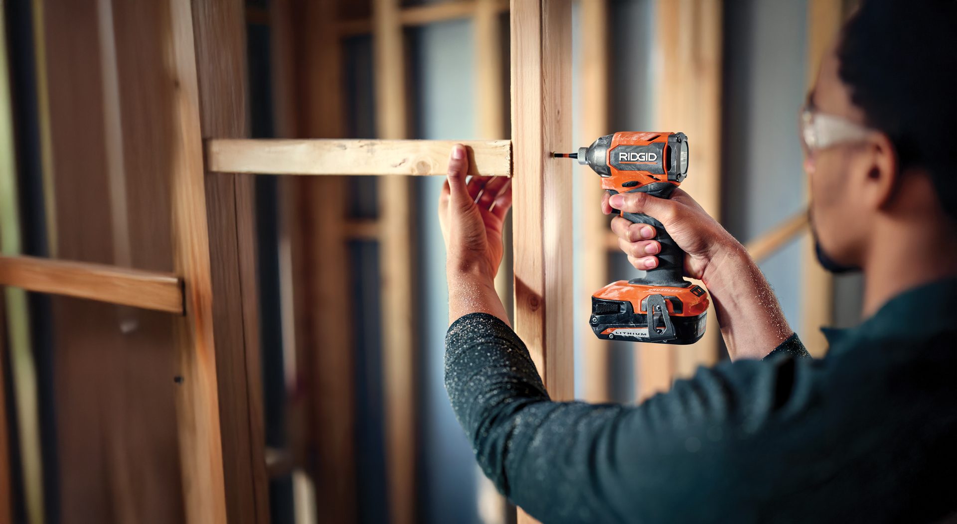 Person using a Ridgid impact driver to secure a wooden beam to a construction frame.