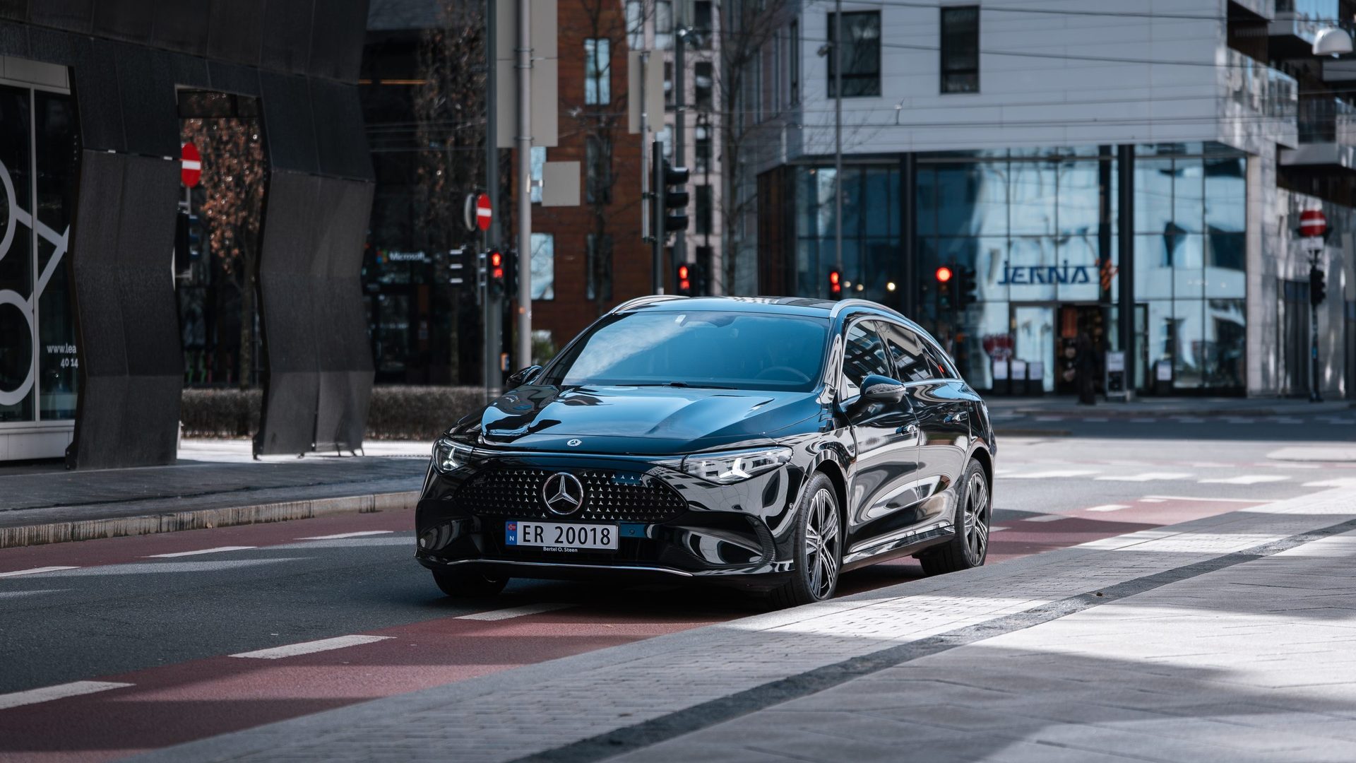 A black Mercedes-Benz EQE SUV is parked on a city street, with modern buildings in the background.