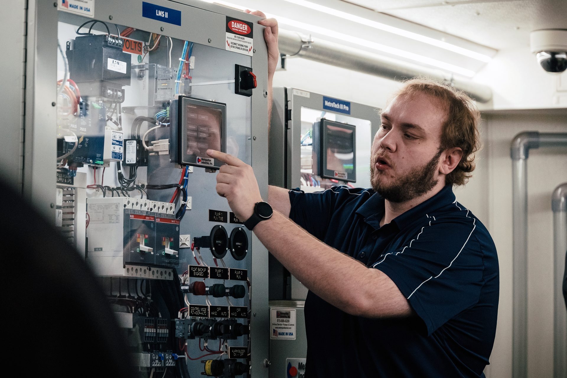 A man with a beard explains controls on an industrial electrical panel.