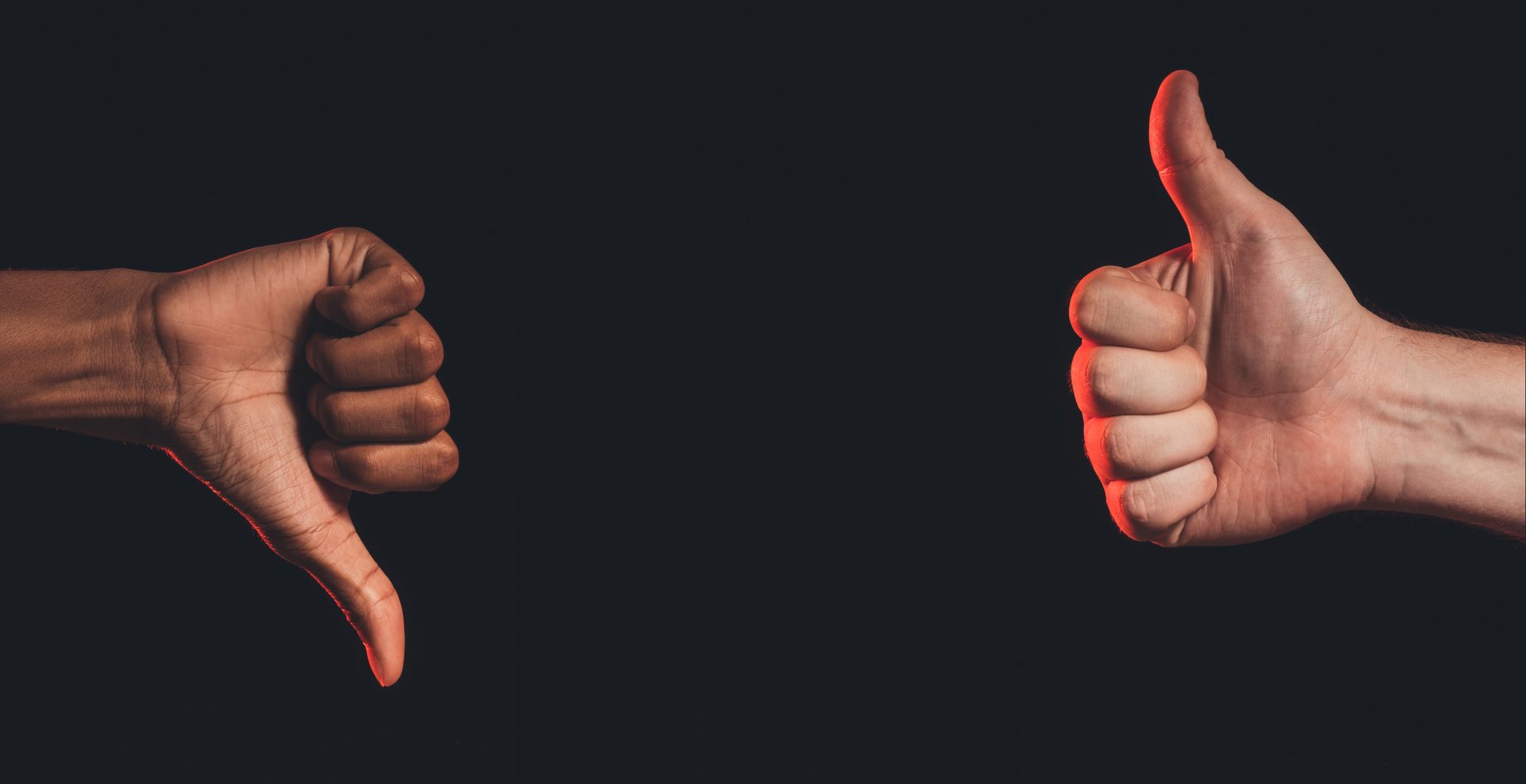 Hands showing thumbs up and thumbs down gestures on a dark background.