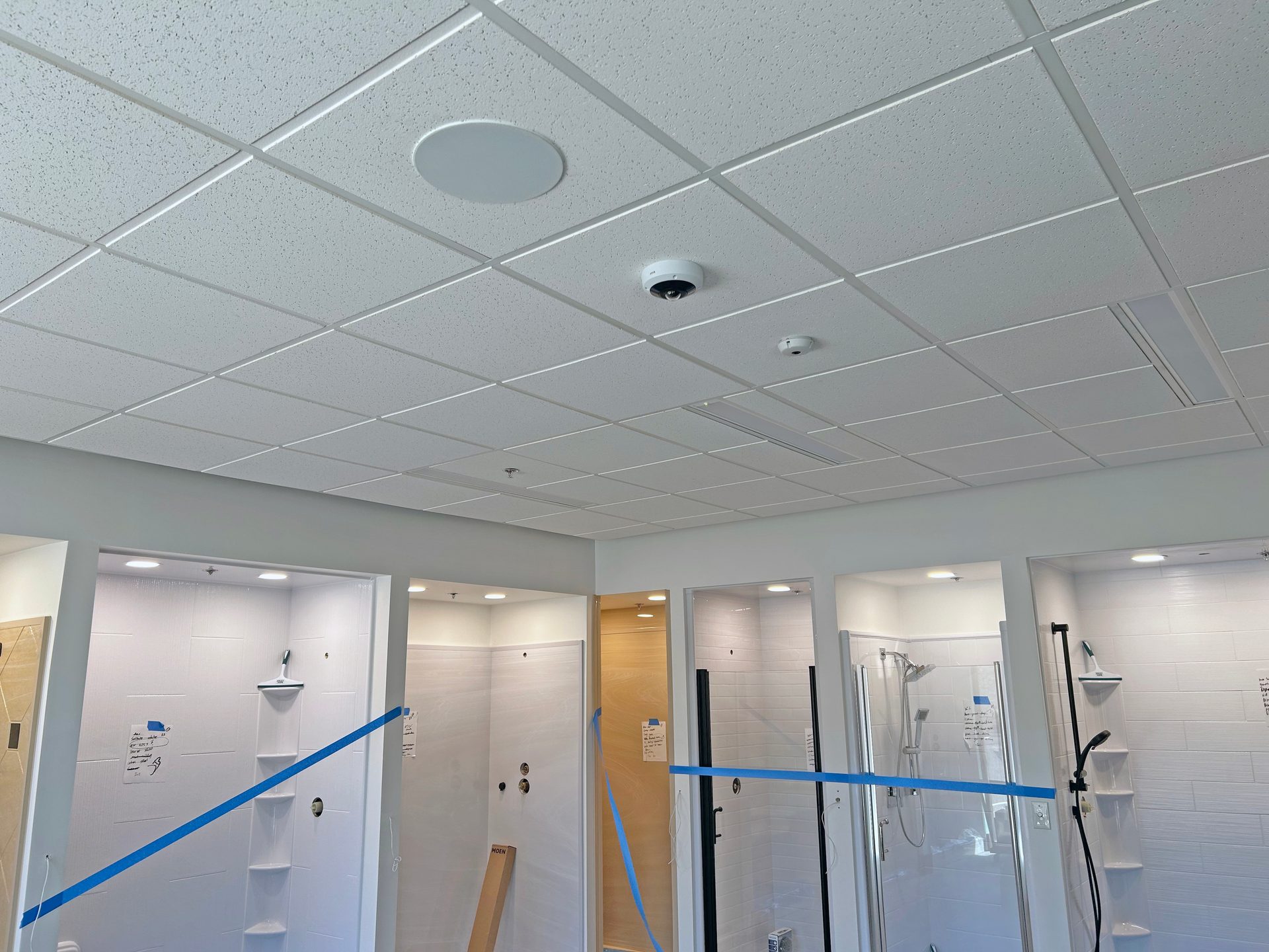 Shower displays with white tiles, blue tape, and a ceiling camera.